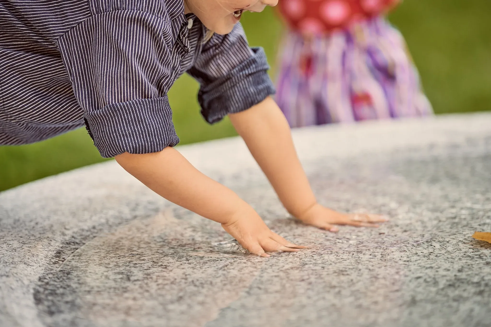 Kind stützt sich auf einen runden hellen Steinbrunnen aus Granit am Hegelplatz