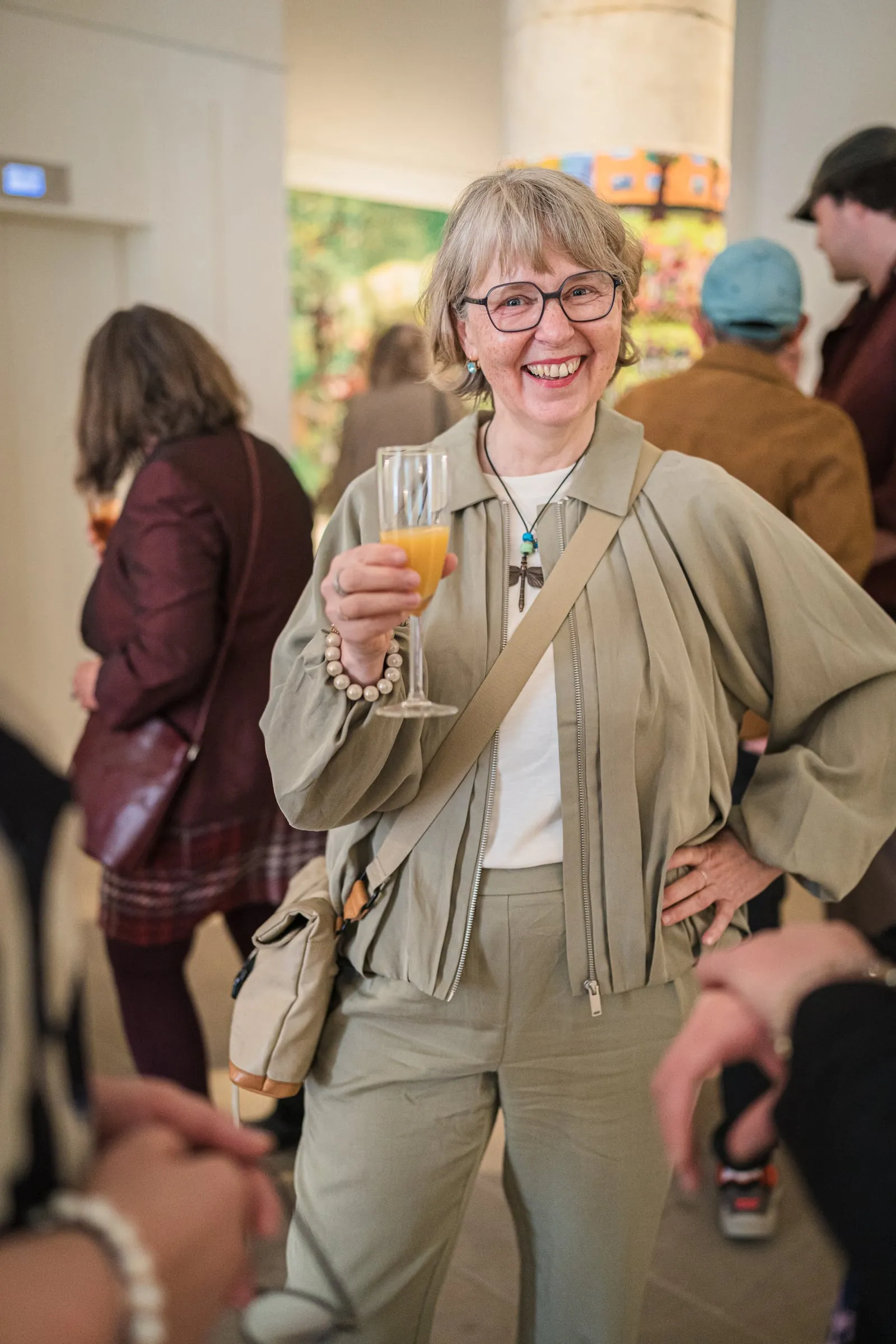 Lächelnde Frau mit Sektglas bei der Ausstellungseröffnung, im Hintergrund Besucher im hellen Galerieraum