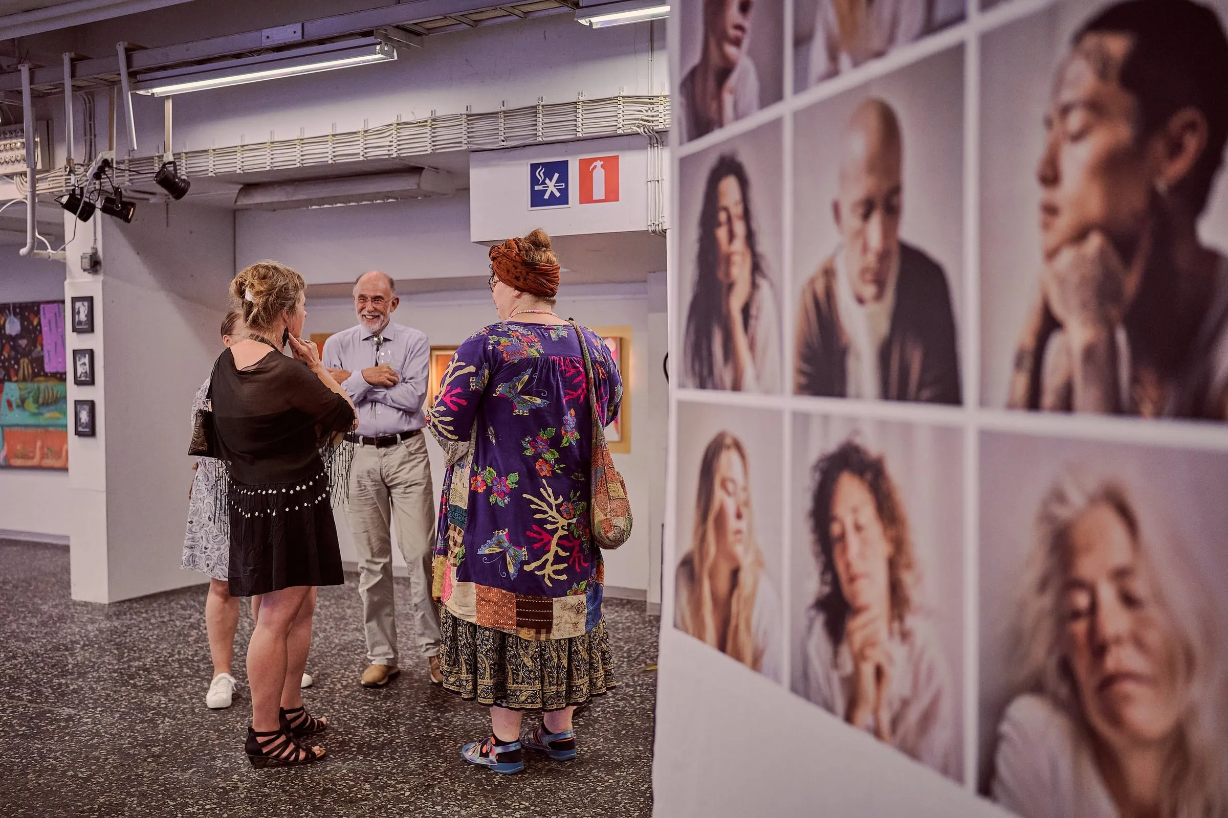 Drei Personen im Gespräch im Ausstellungsraum, rechts eine Wand mit gerahmten Porträtfotografien