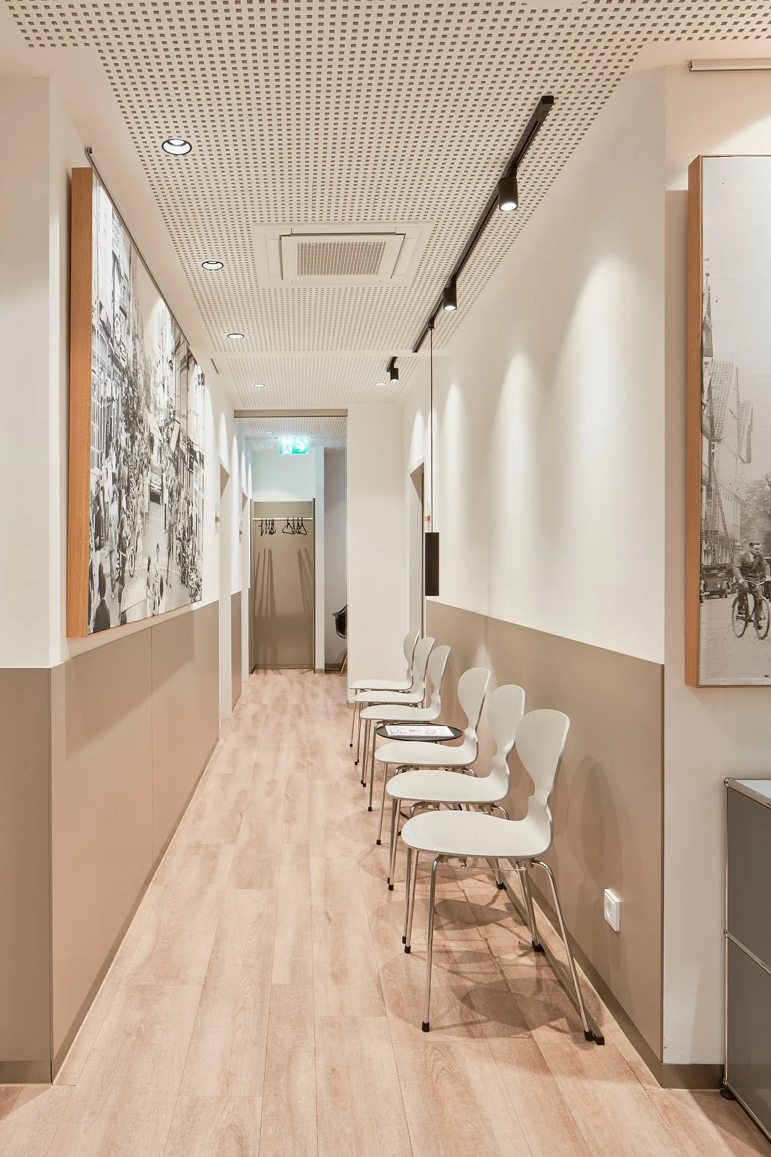 Heller Wartebereich der Augenpraxis Celle, weiße Stühle entlang des Flurs, Holzboden, gerahmte Schwarzweißfotografien an der Wand
