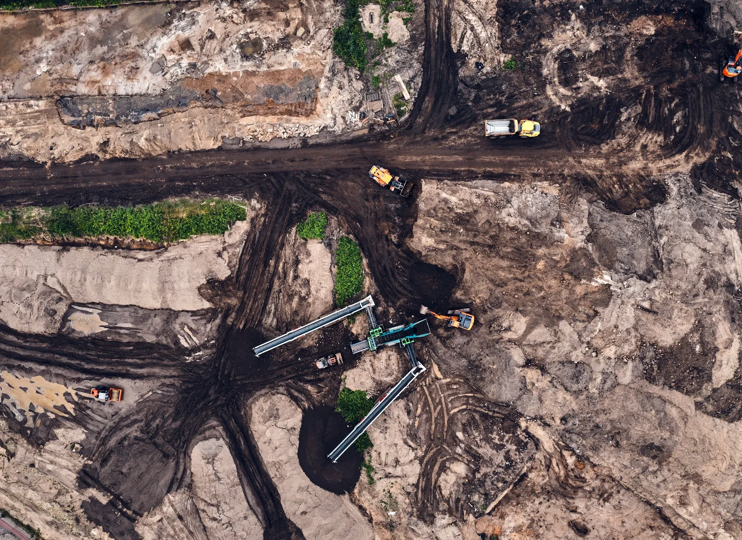 Senkrechte Luftaufnahme einer Erdbaustelle mit Gerät, Förderband und ausgehobenen Sandflächen