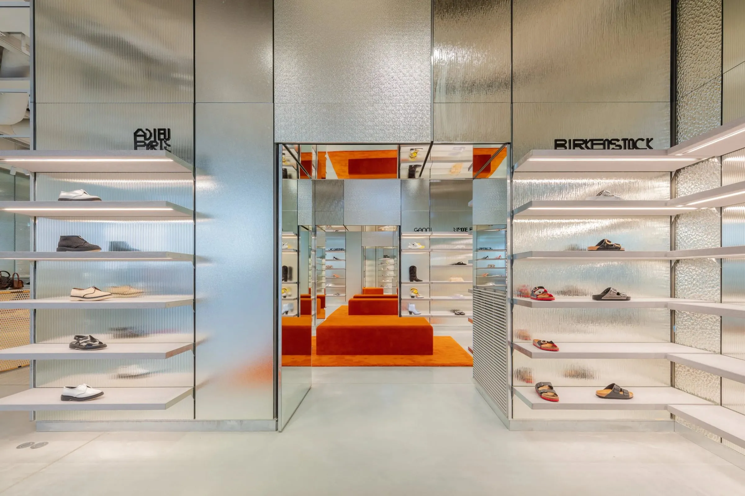 Schuhabteilung in den Galeries Lafayette mit verspiegelten Wänden, hellen Wandregalen und rotem Eingangsbereich, Innenraum