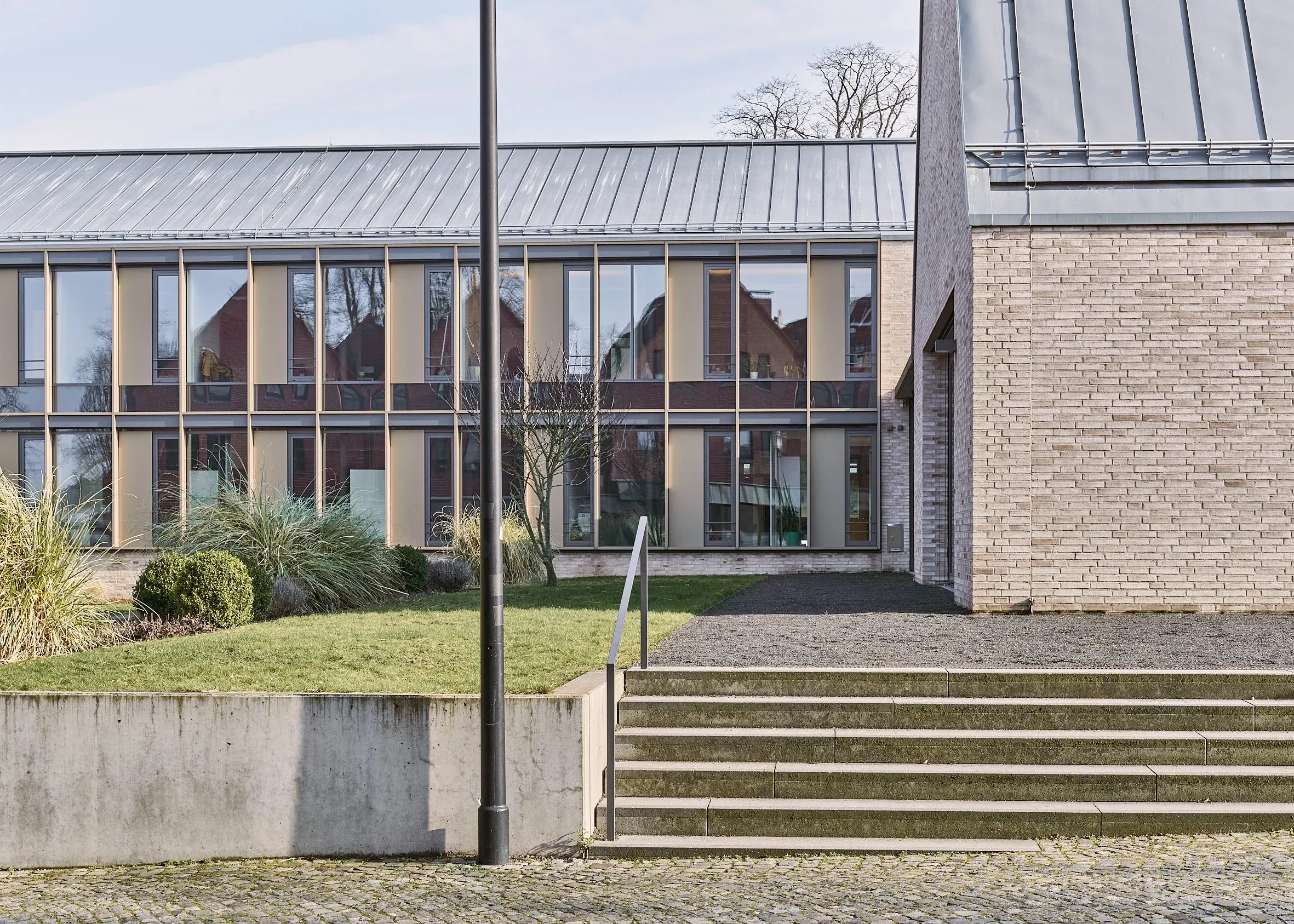 Außenaufnahme der gläsernen Fassade des Rathauses Bissendorf, zweigeschossige Fensterbänder, davor Rasen, Treppe und Geländer