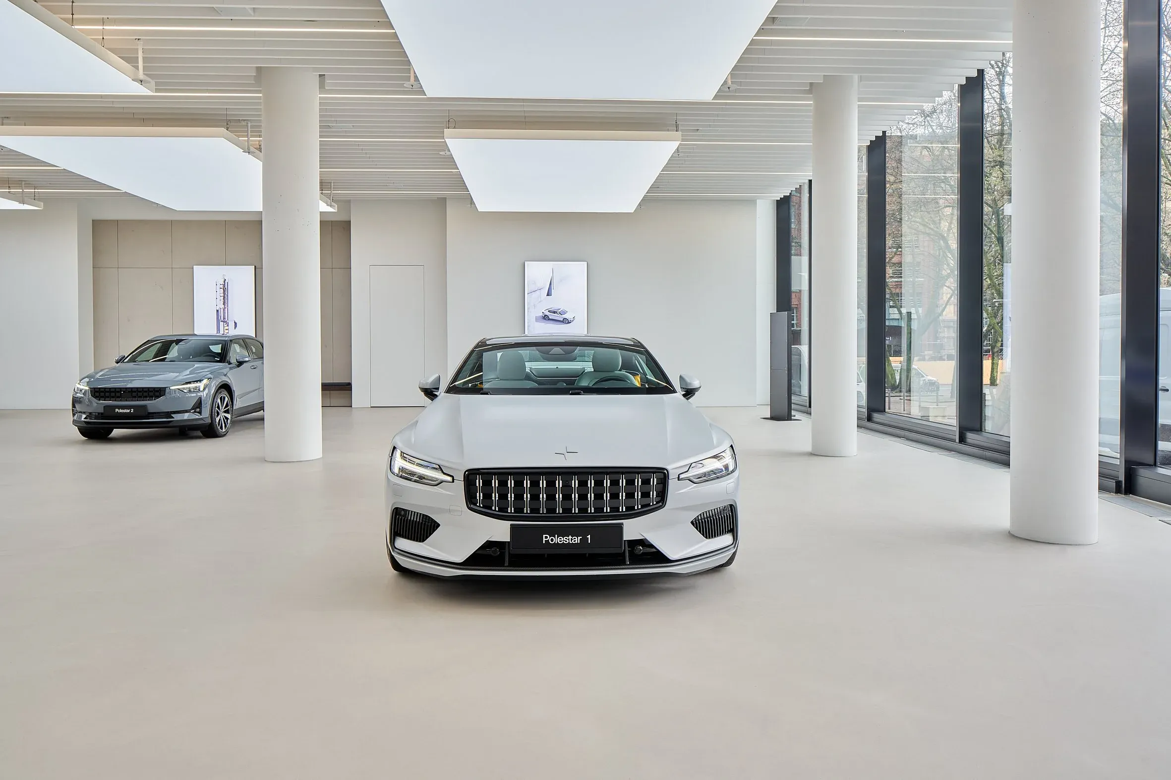 Innenraum des Showrooms, weißer Polestar 1 frontal zwischen schlanken Säulen, zweites Fahrzeug im Hintergrund