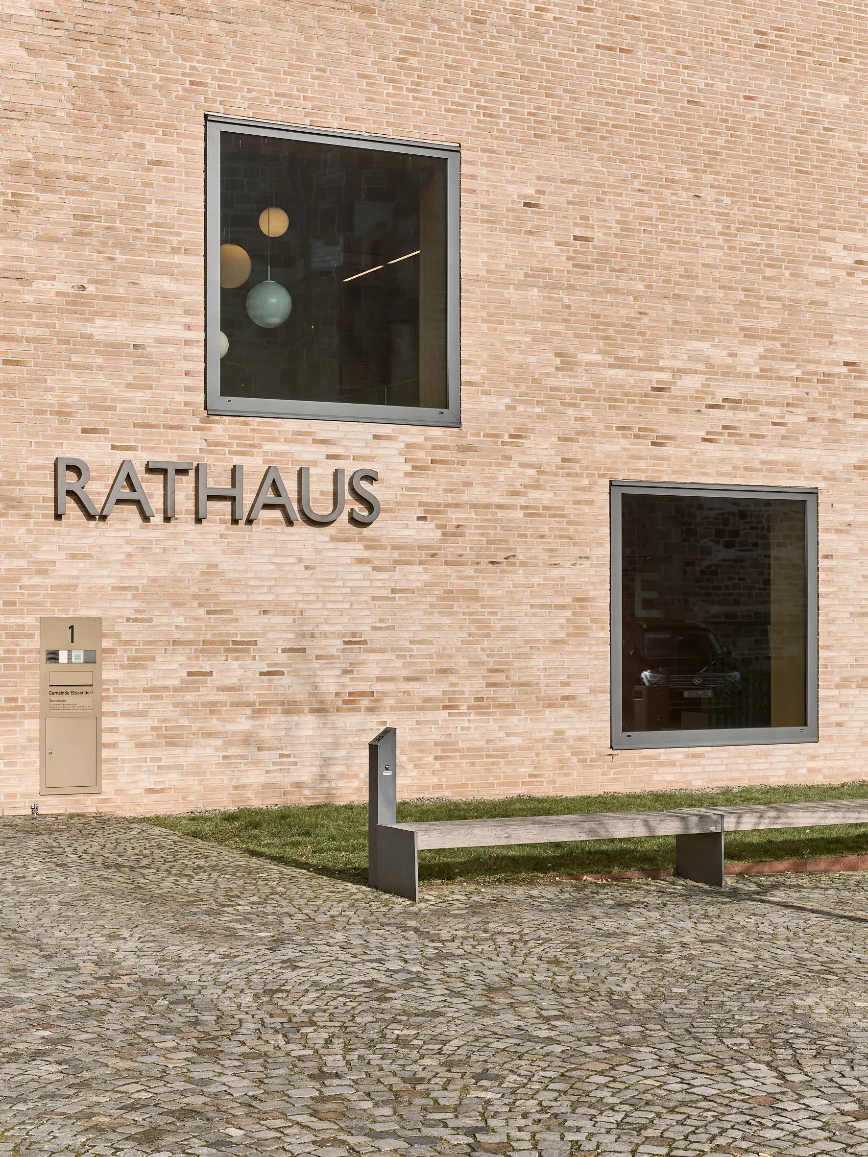 Detail der Klinkerwand mit Schriftzug Rathaus, zwei quadratischen Fenstern und einer Sitzbank auf gepflastertem Vorplatz