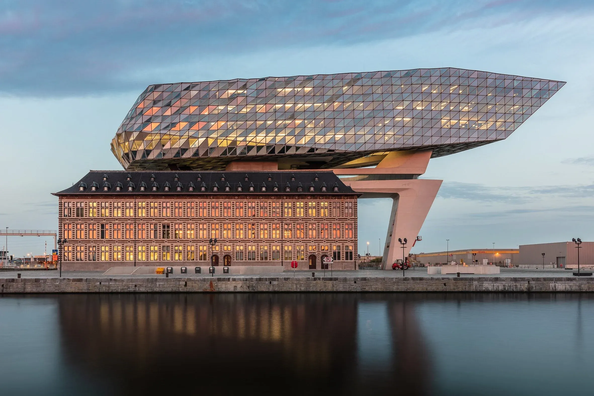 Gesamtansicht aus der Distanz über das Wasser, beleuchtetes Hafenhaus mit gläsernem Aufbau über dem Altbau in der Abenddämmerung mit Spiegelung