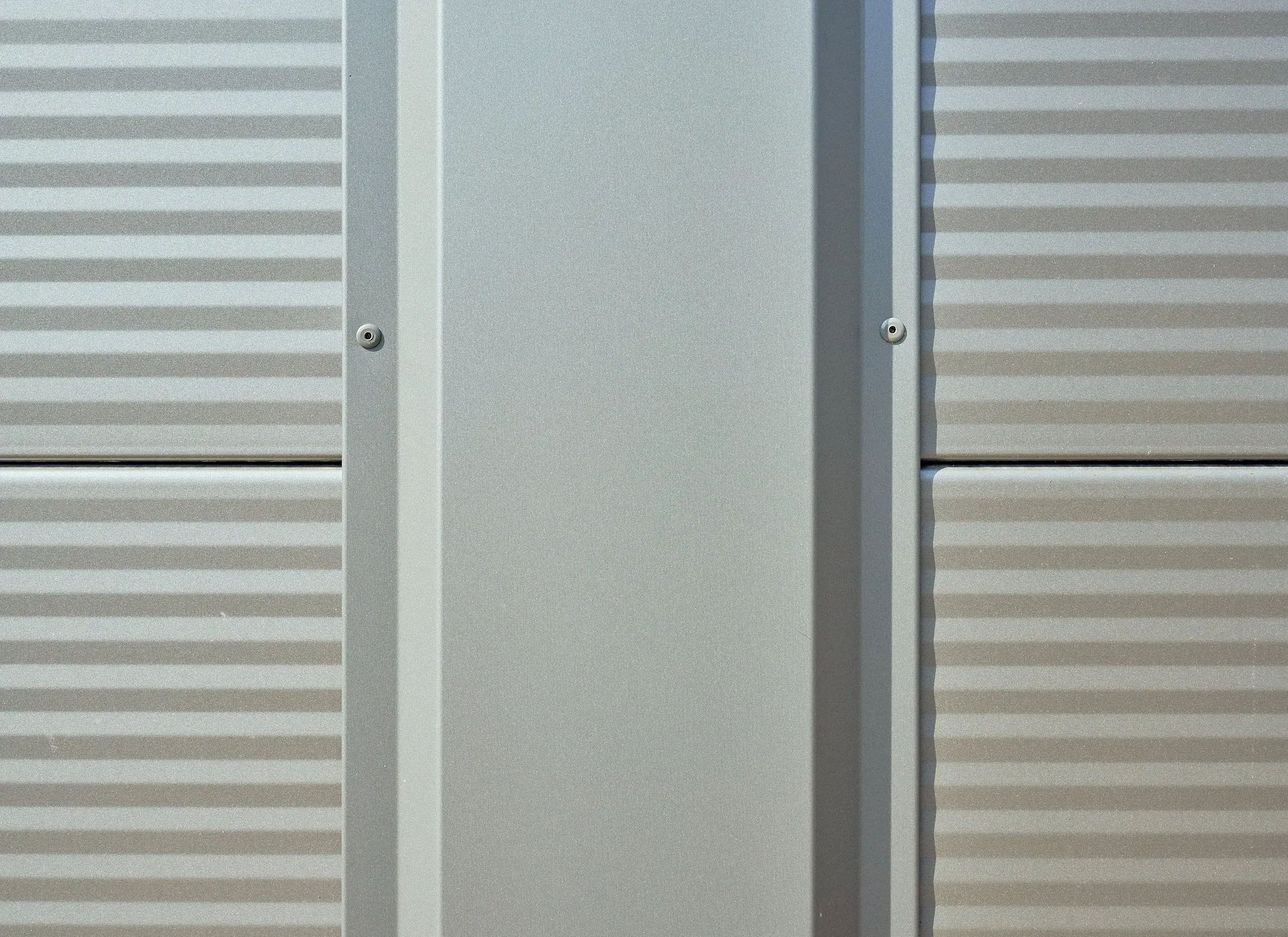 Detail der hellen Fassadenverkleidung mit profiliertem Trapezblech und glatter Pfeilerblende, Verschraubungen sichtbar