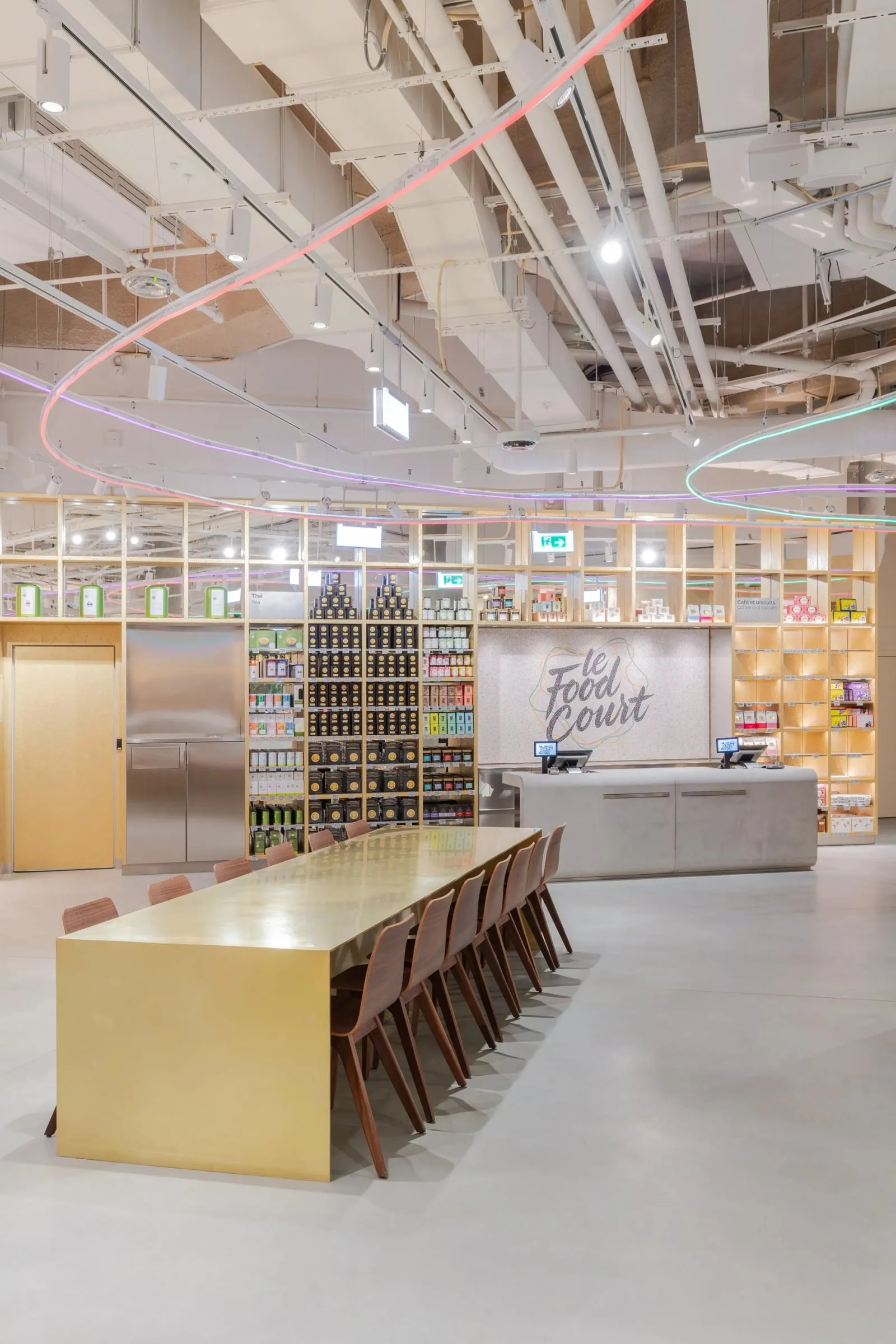 Food-Court-Bereich mit langer goldener Tafel, Holzstühlen und Regalwand, Innenraum, Tageslicht