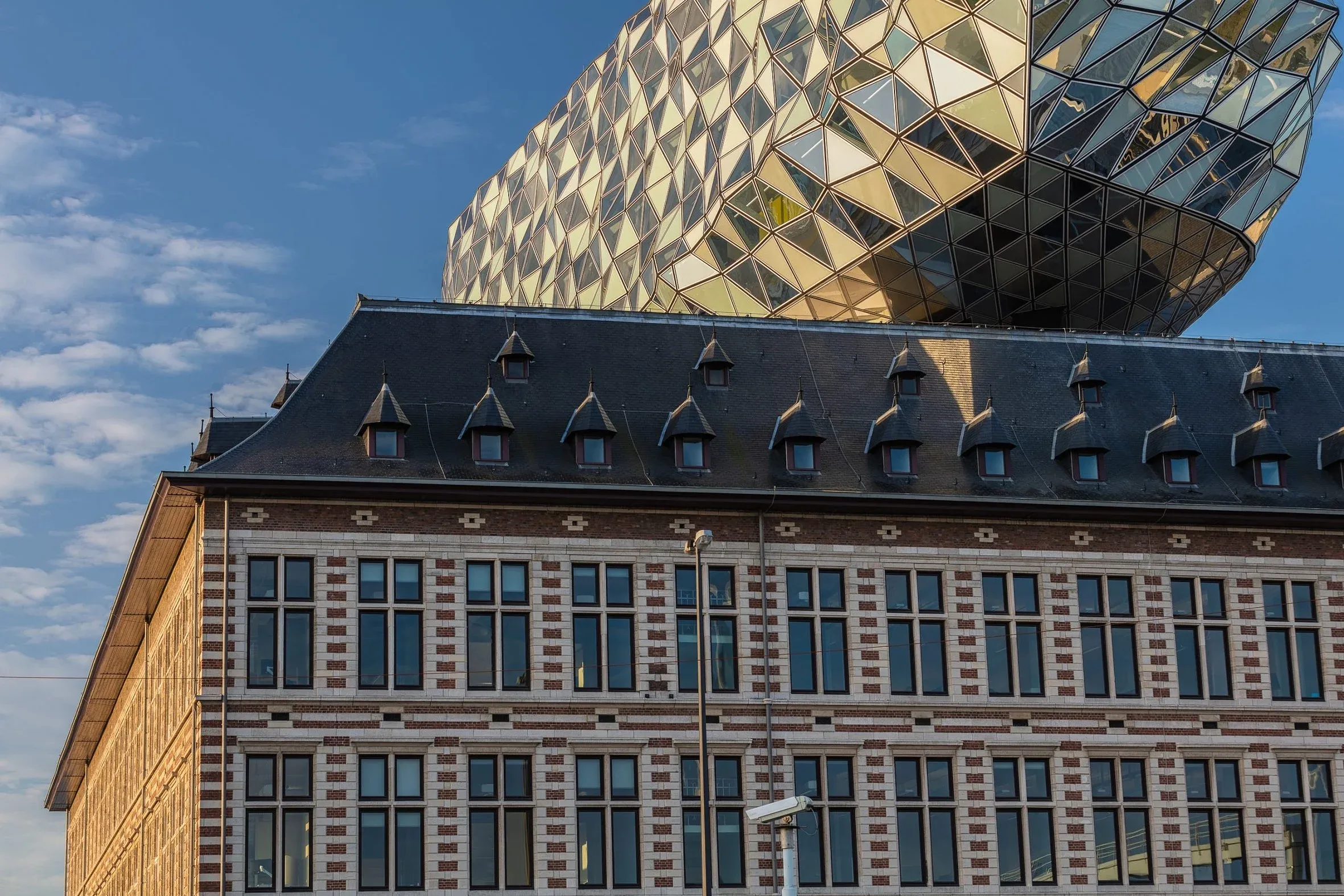 Detail im Abendlicht, der golden spiegelnde gläserne Aufbau ragt über das Schieferdach und die Backsteinfassade des Altbaus