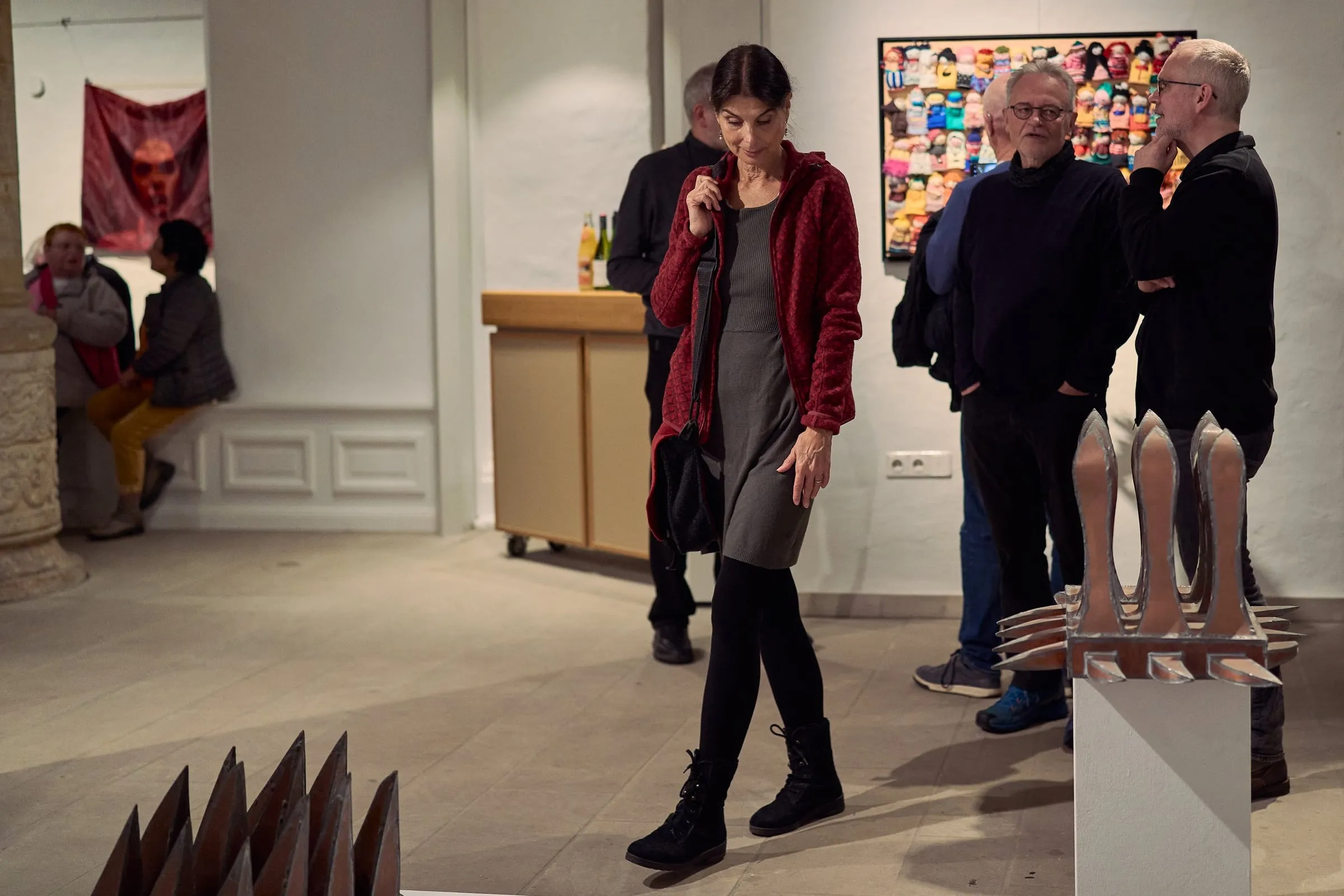 Besucherinnen und Besucher im Ausstellungsraum betrachten metallene Skulpturen und Werke an der Wand