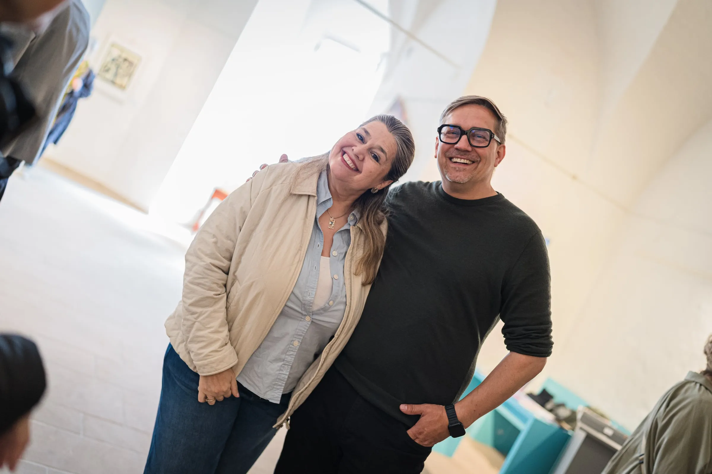 Eine Frau und ein Mann lehnen lachend aneinander im hellen Ausstellungsraum