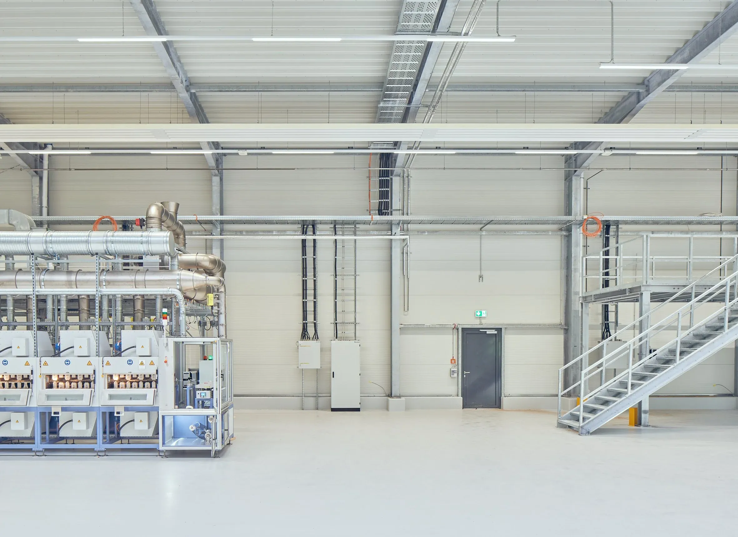 Innenansicht der Produktionshalle mit Maschinenreihe links, Stahltreppe rechts und Leuchtbändern an der Decke