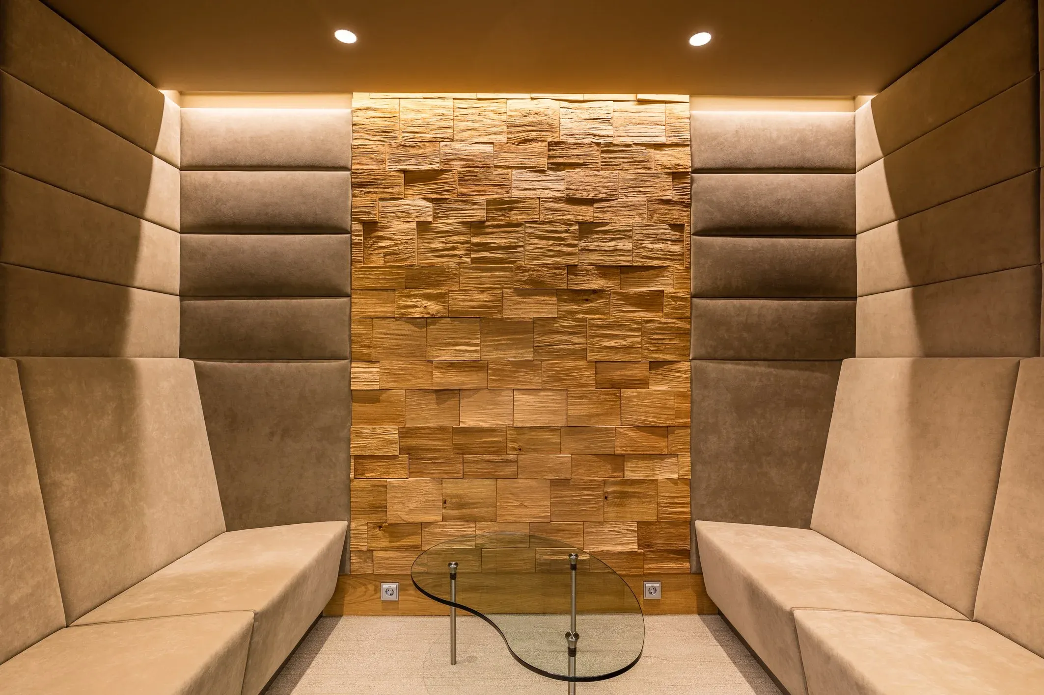 Innenraum mit gepolsterten Sitznischen, beleuchteter Holzwand aus versetzten Klötzen und kleinem Glastisch