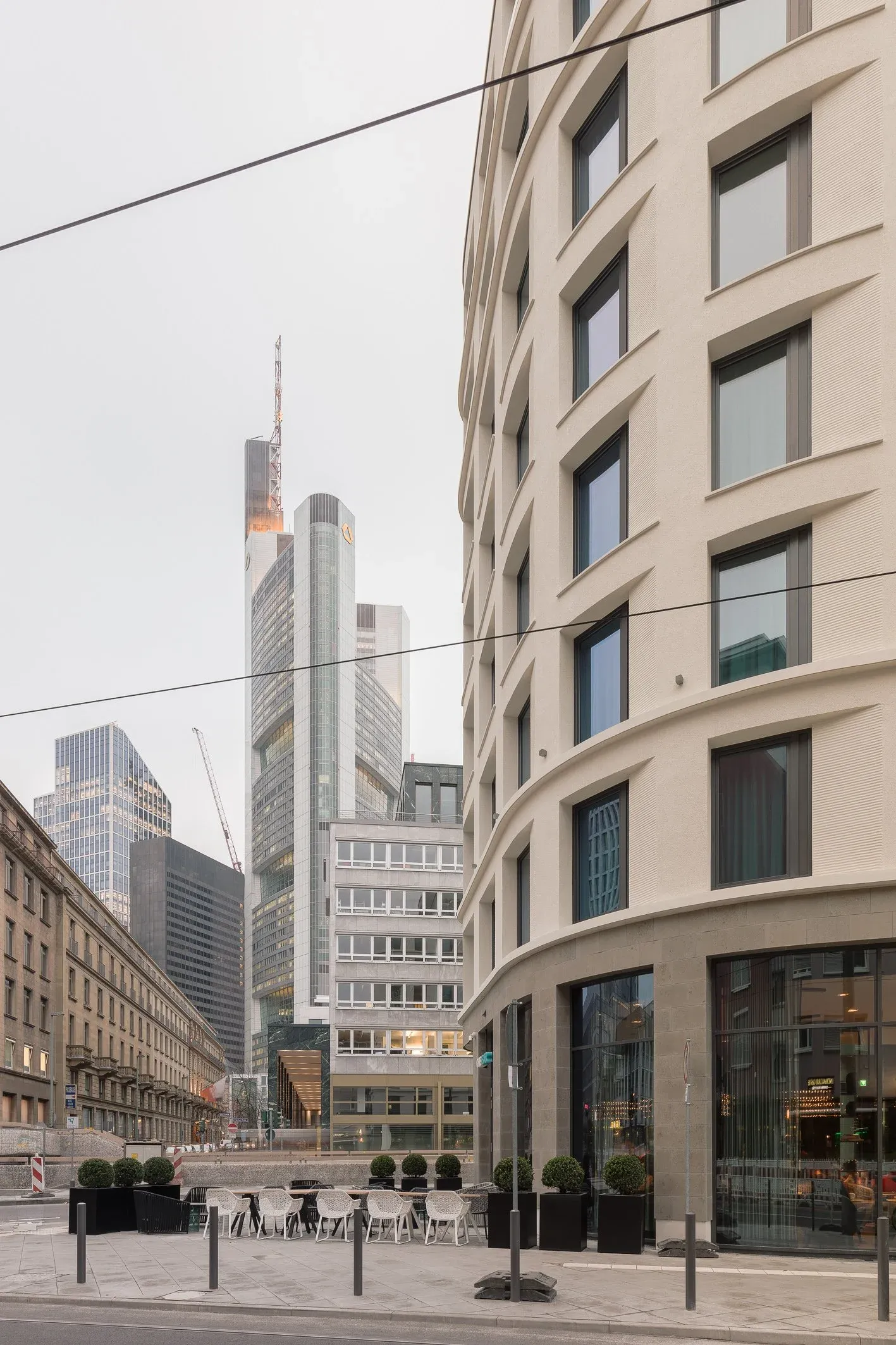 Blick aus der Frankfurter Straße auf die gerundete Gebäudeecke des Motel One, im Hintergrund Hochhäuser der Skyline