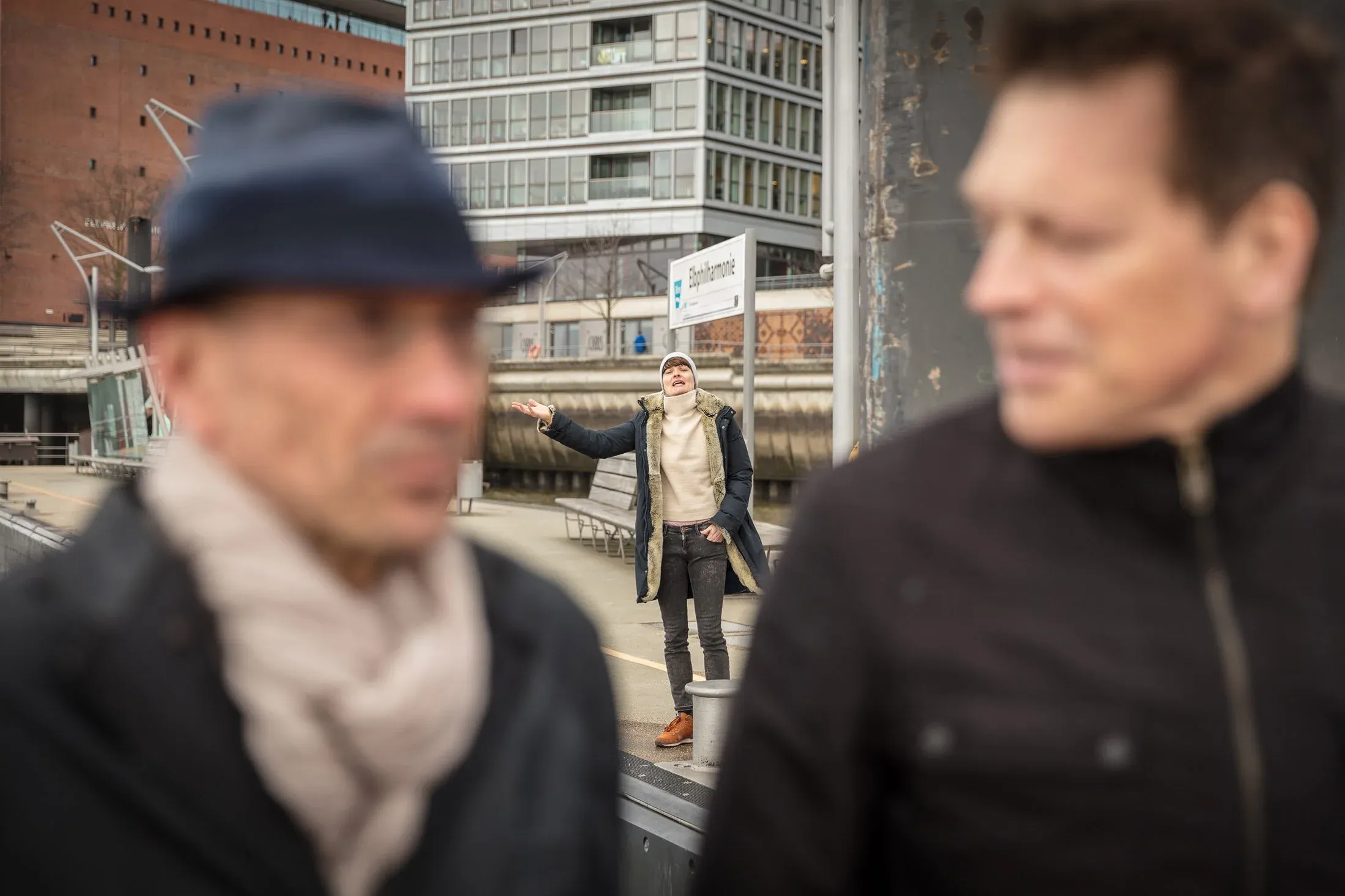 Zwei Männer im Vordergrund, dahinter gestikulierende Person vor Gebäuden der HafenCity