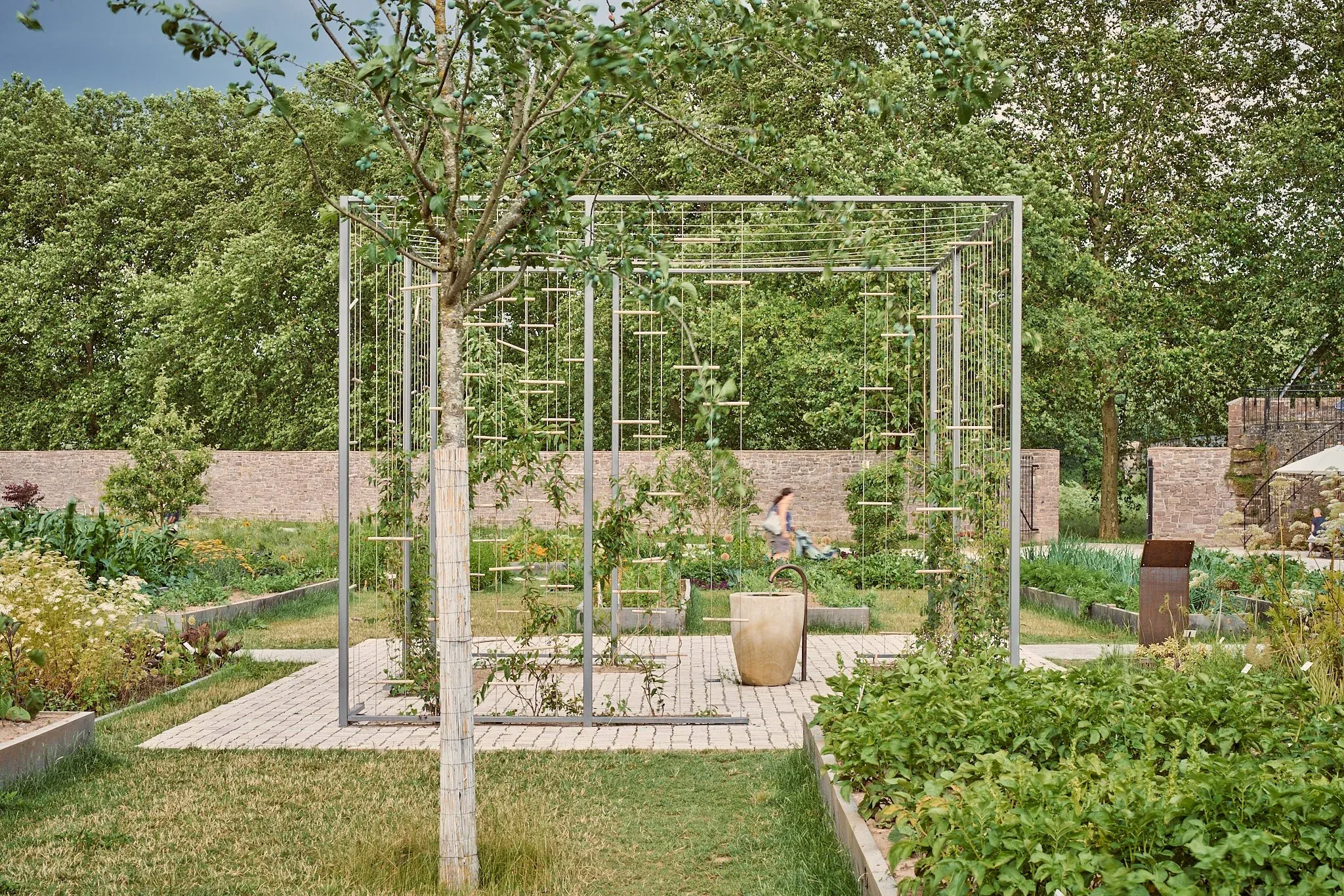 Gerüstartige Stahlkonstruktion über einem Beet im Remtergarten, Bäume und alte Mauer im Hintergrund