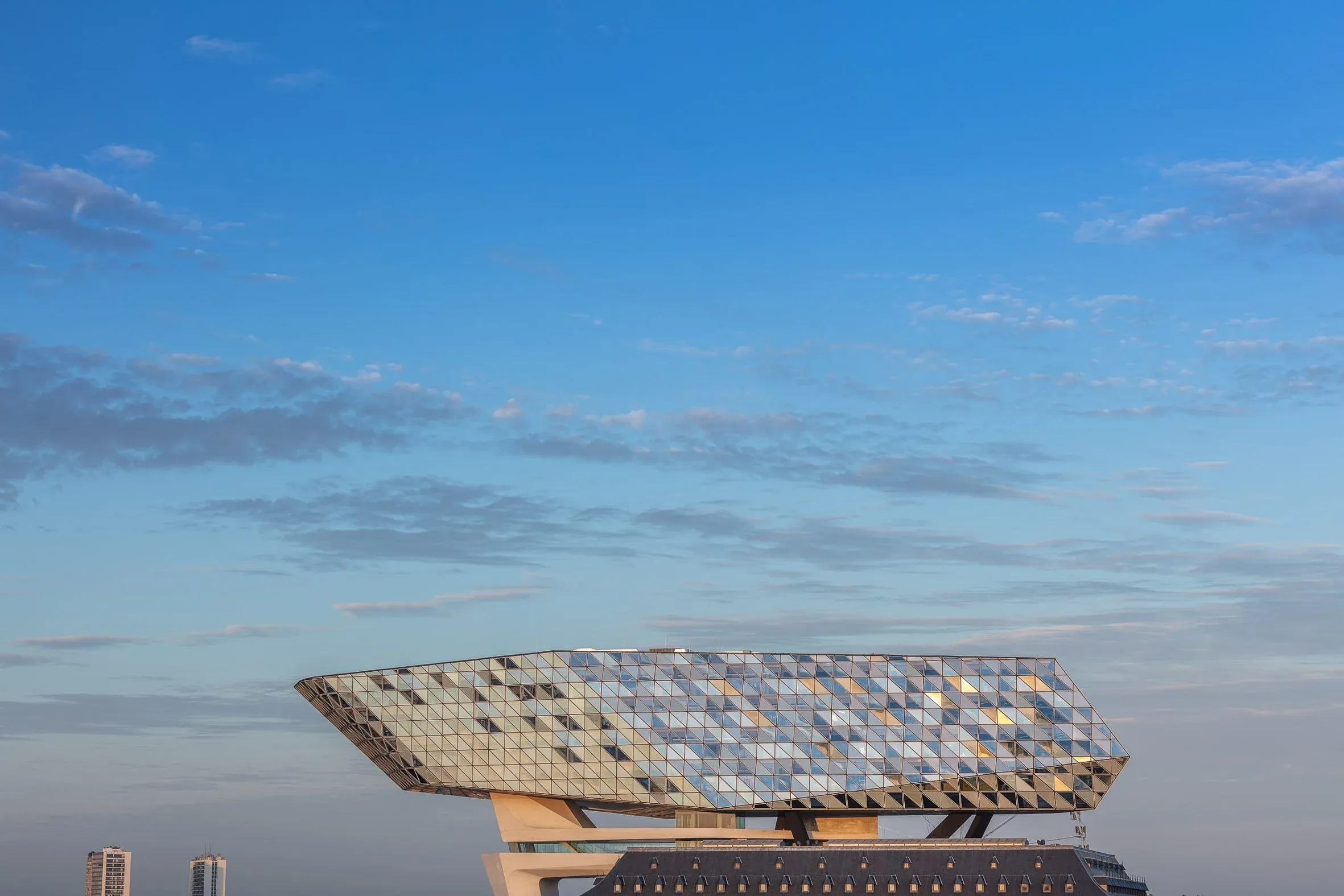 Der facettierte gläserne Baukörper des Hafenhauses ragt im Morgenlicht vor weitem Himmel über den Altbau hinaus