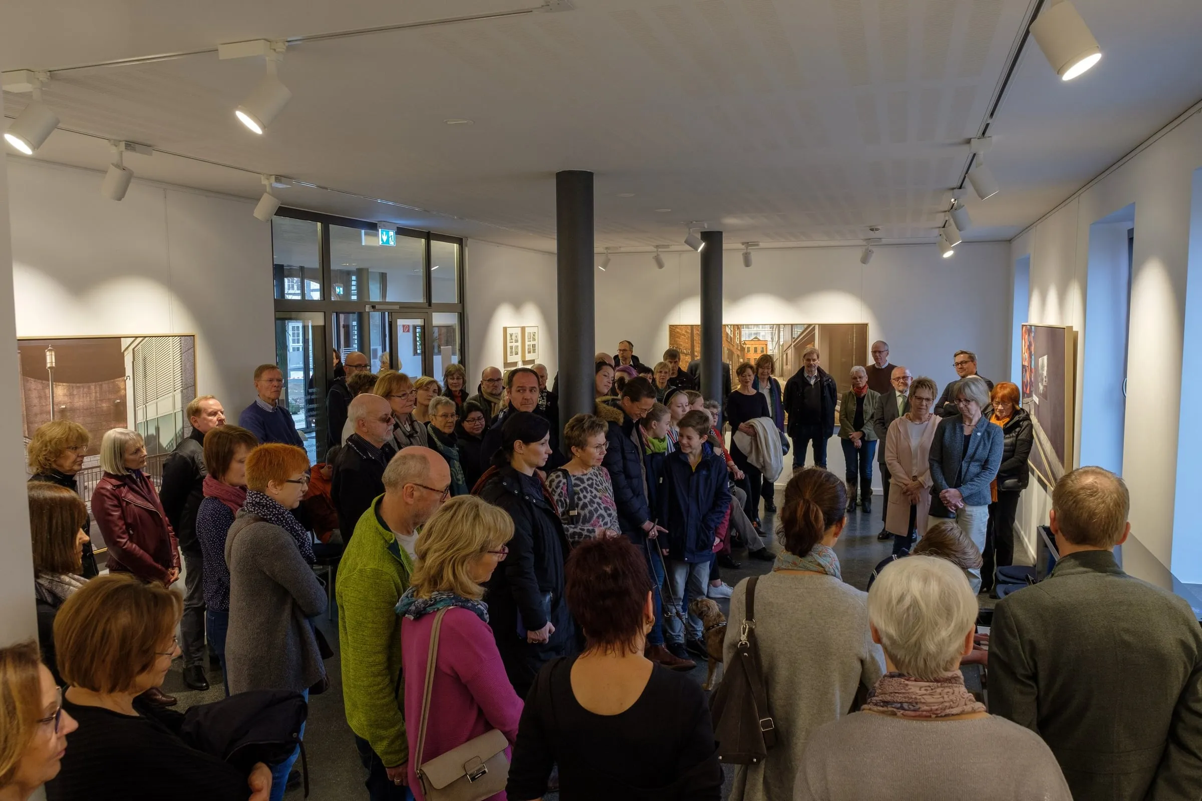 Dicht gedrängtes Publikum bei der Eröffnung im hellen Galerieraum mit Fotografien an den Wänden