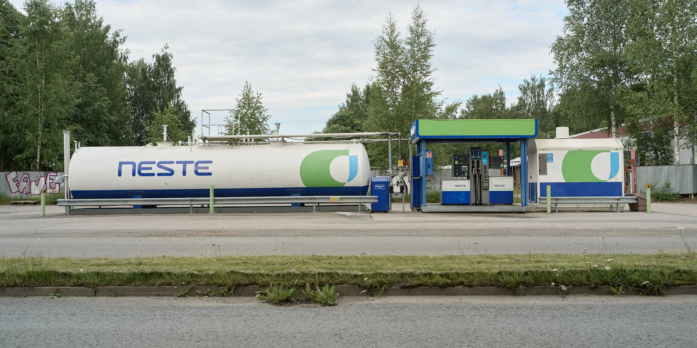 Small petrol station with a white tank in front of green trees