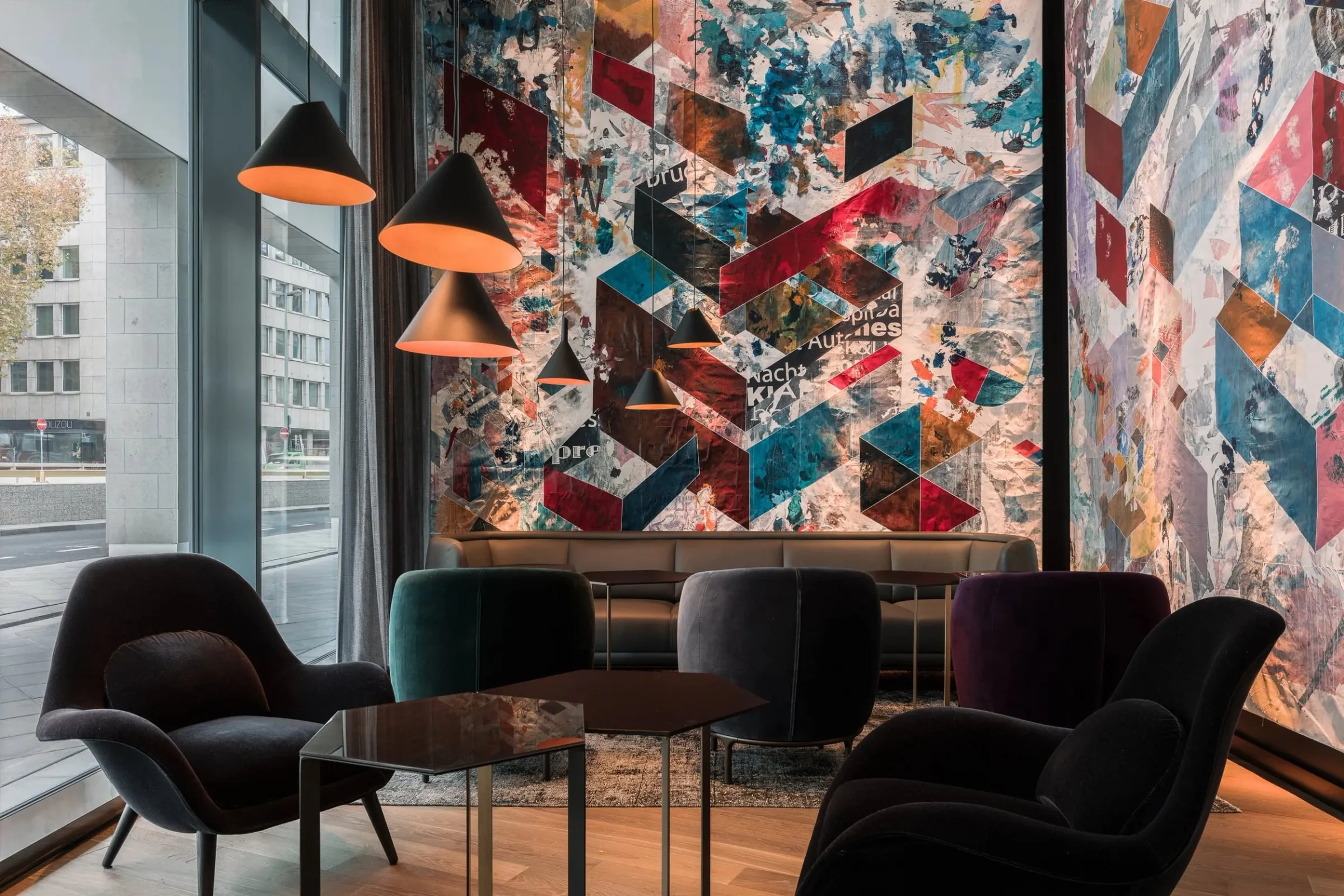Lounge innen mit dunklen Sesseln, Hängeleuchten und großem abstraktem Wandbild in kräftigen Farben, Fensterfront links