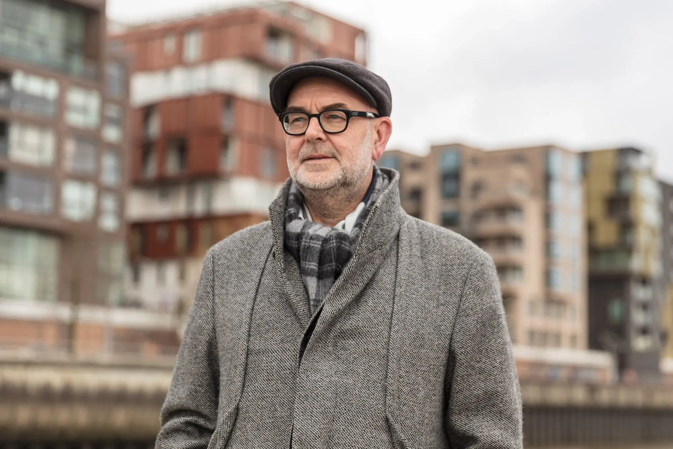 Porträt eines Mannes mit Brille und Schiebermütze, im Hintergrund Wohnbauten der HafenCity
