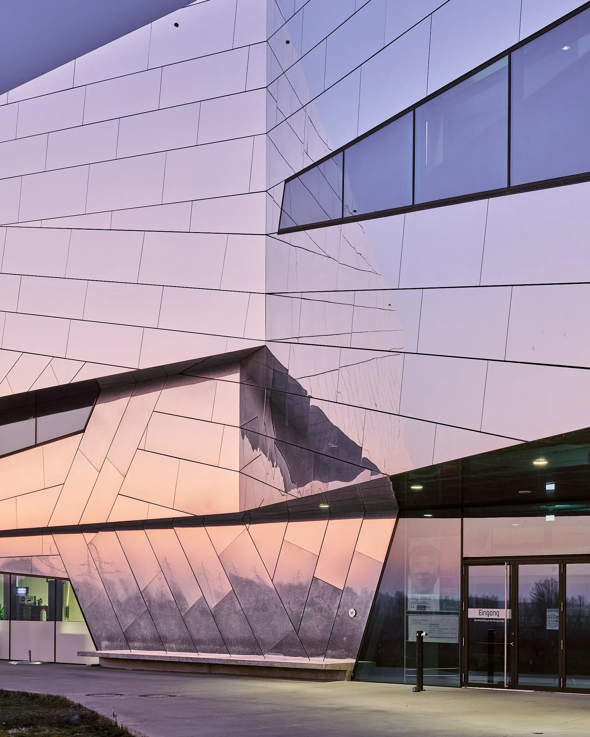 Eingangsbereich des Paläon, facettierte Metallfassade mit gläserner Eingangstür im Abendlicht