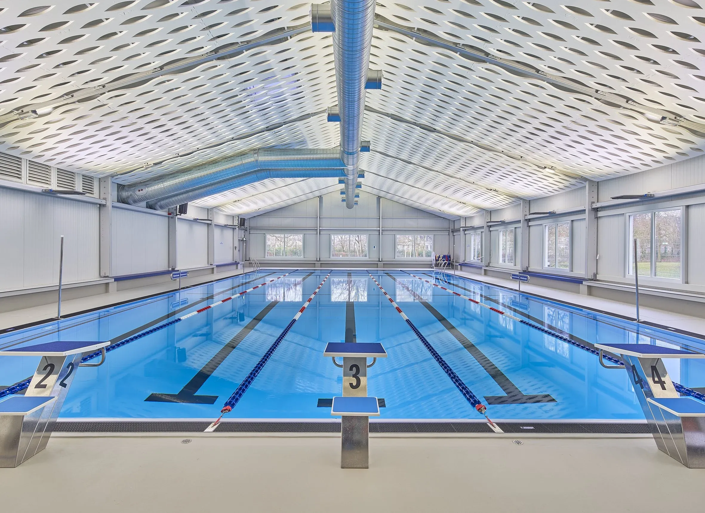 Innenaufnahme einer Schwimmhalle, Becken mit Startblöcken unter heller Zeltdachkonstruktion von HTS Tentiq