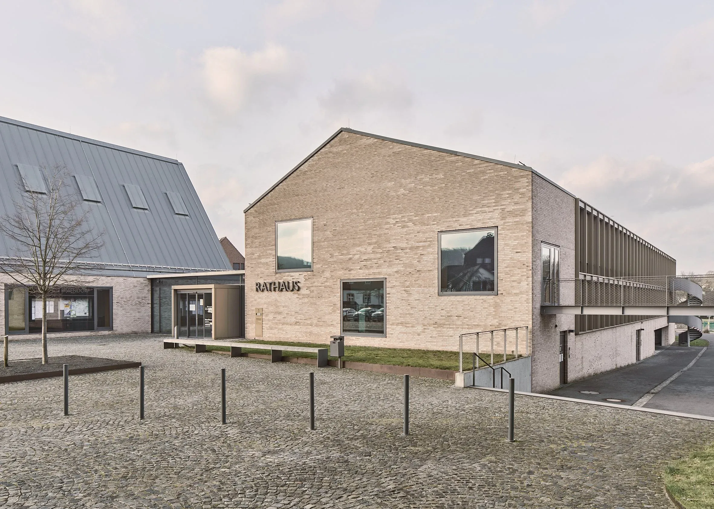 Außenansicht des Rathauses Bissendorf mit Klinkergiebel und Schriftzug Rathaus, gepflasterter Vorplatz, Metalldach und Rampe rechts