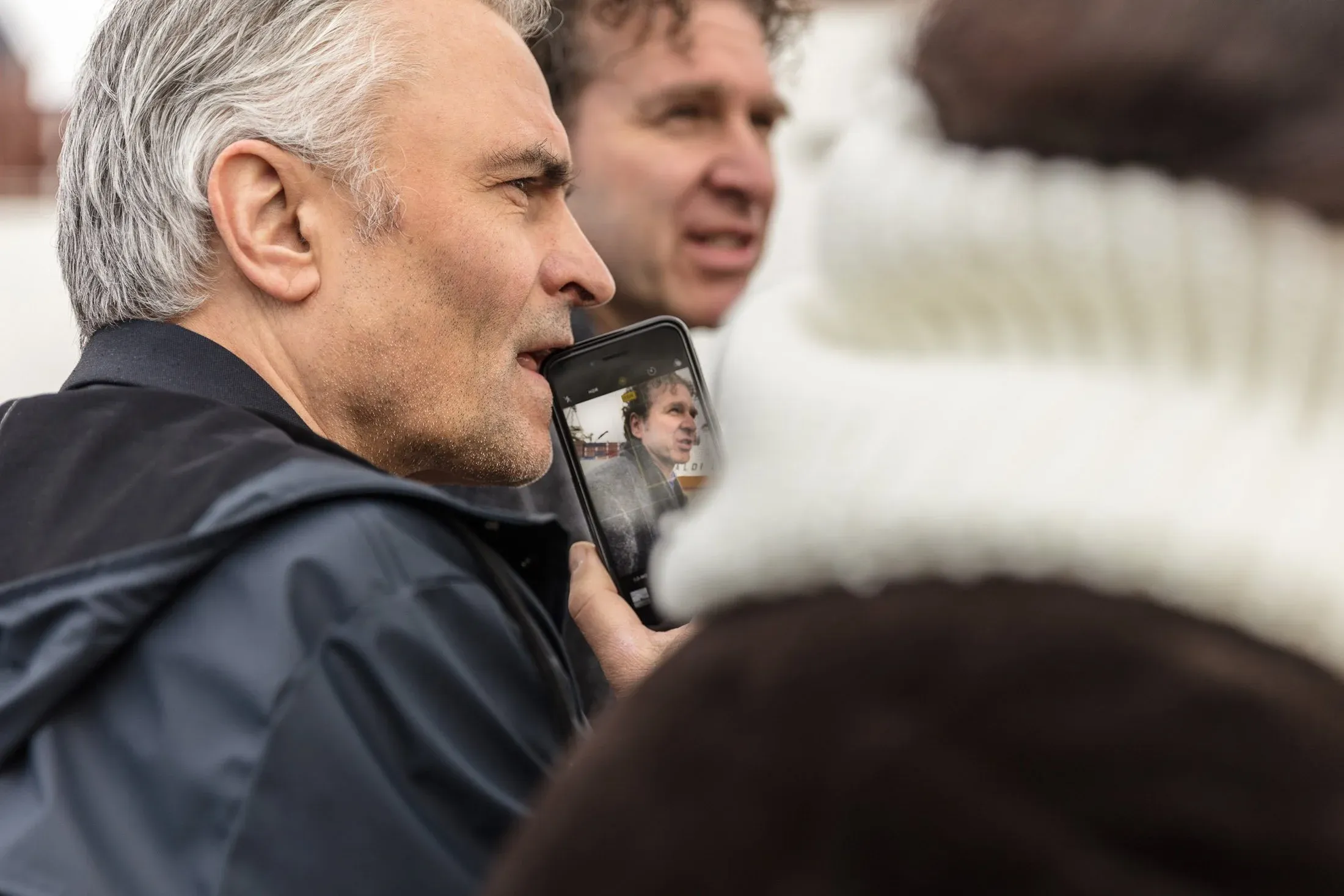 Mann filmt mit dem Smartphone, im Display spiegelt sich ein Gesprächspartner