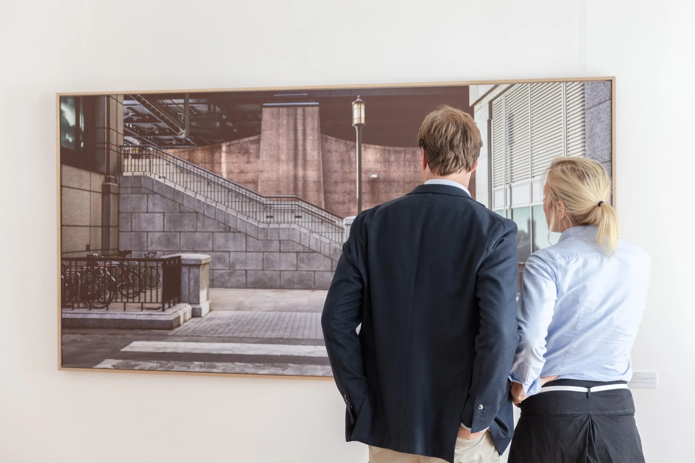 Mann und Frau von hinten betrachten großformatige gerahmte Fotografie einer steinernen Treppe