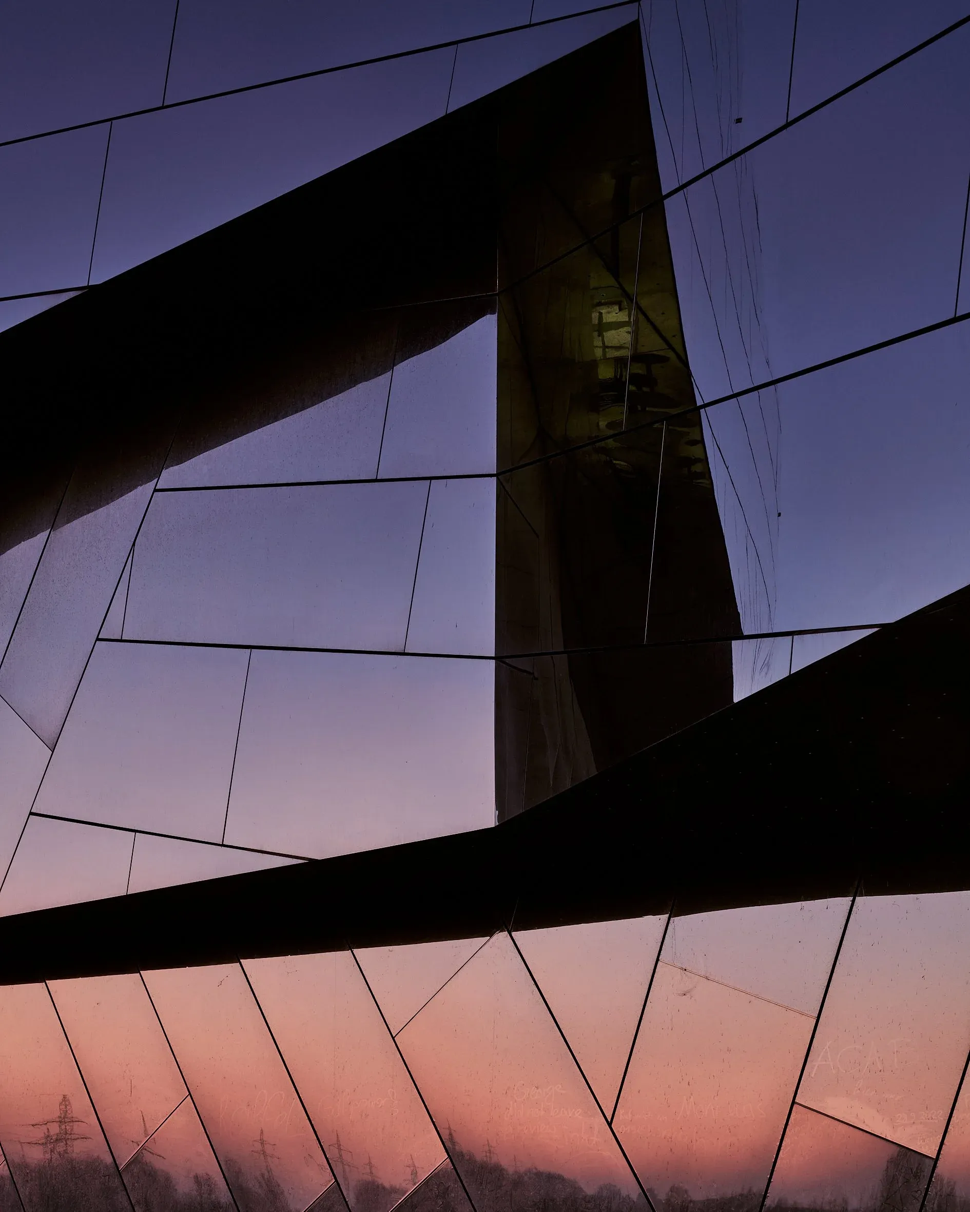 Detail der gefalteten Fassade des Paläon, dunkle Glasflächen spiegeln den Abendhimmel, fast abstrakt