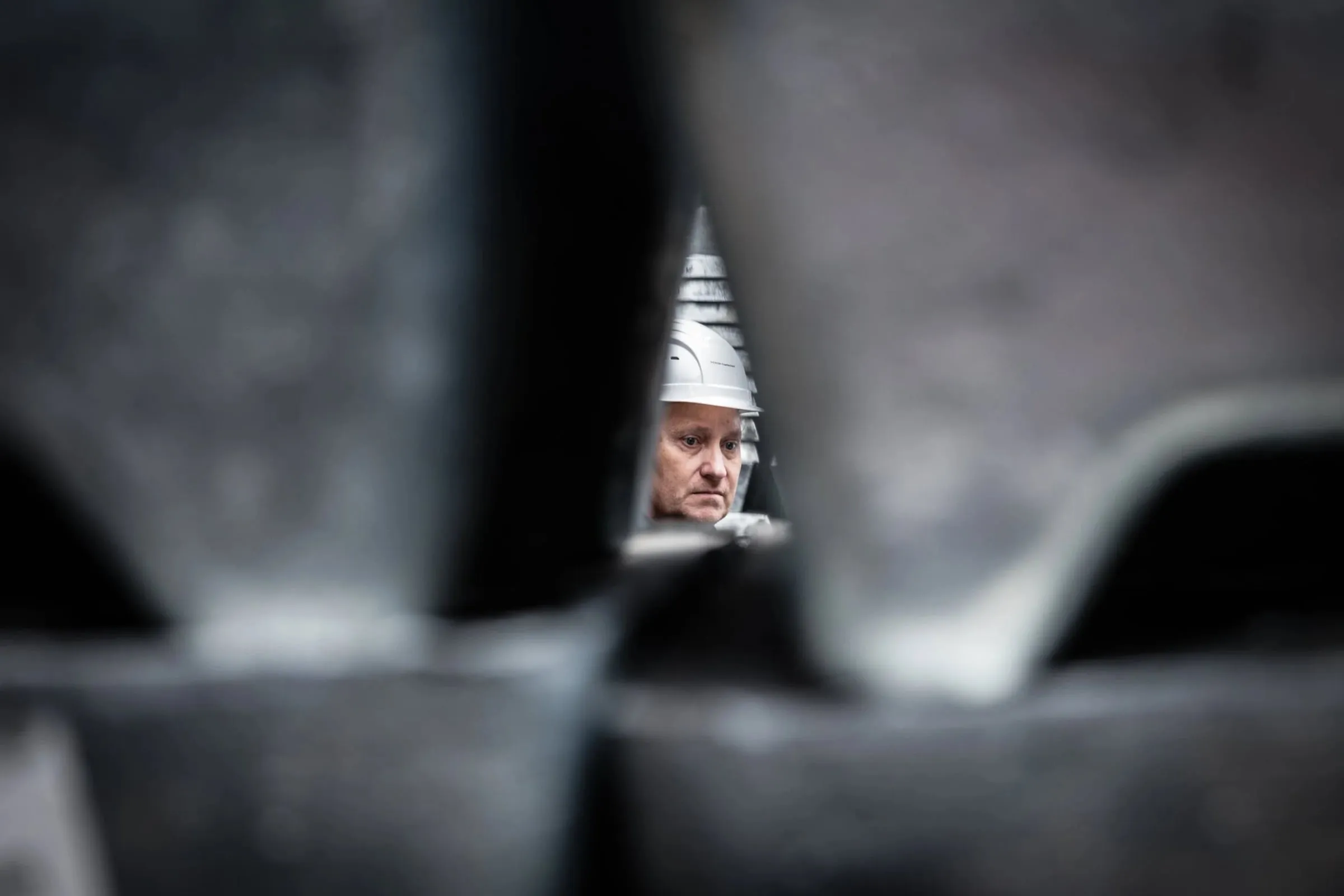 Arbeiter mit weißem Schutzhelm blickt durch einen schmalen Spalt zwischen gestapelten Zinkblöcken, Detail
