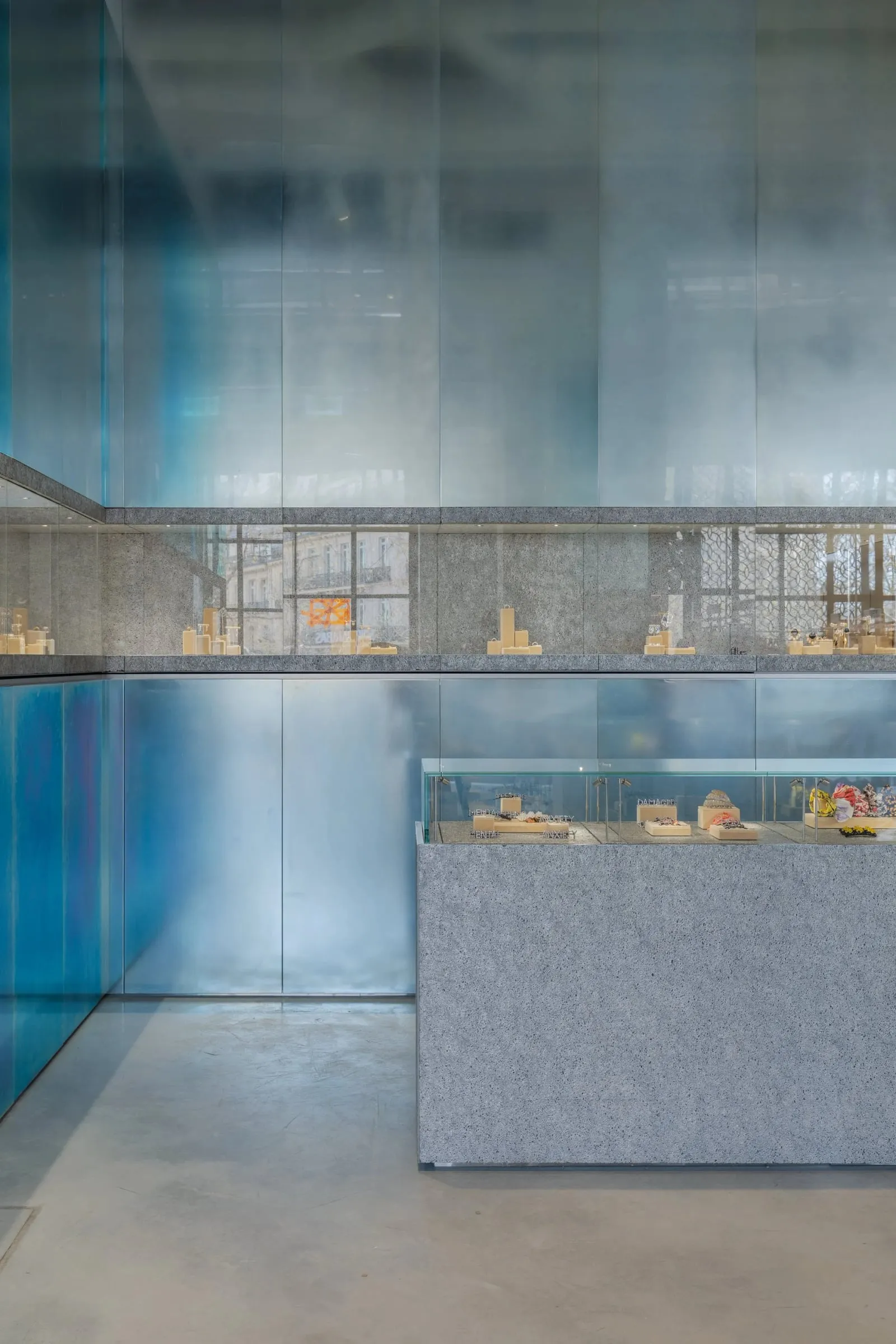 Vitrine mit Schmuck vor großer blau schimmernder Glaswand, Detail im Innenraum