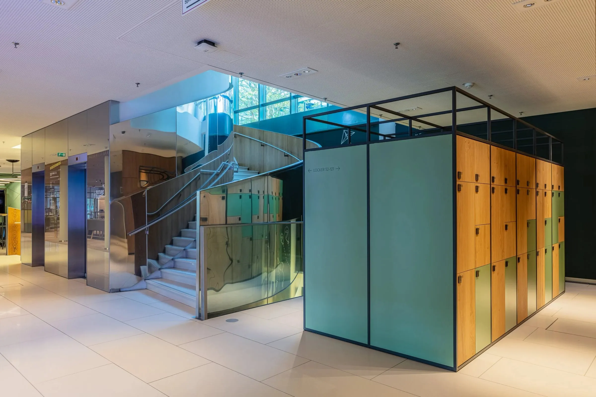 Innenraum mit verglaster Treppe und Schließfachschränken in Holz und Grün im hellen Foyer der Arbeitswelt