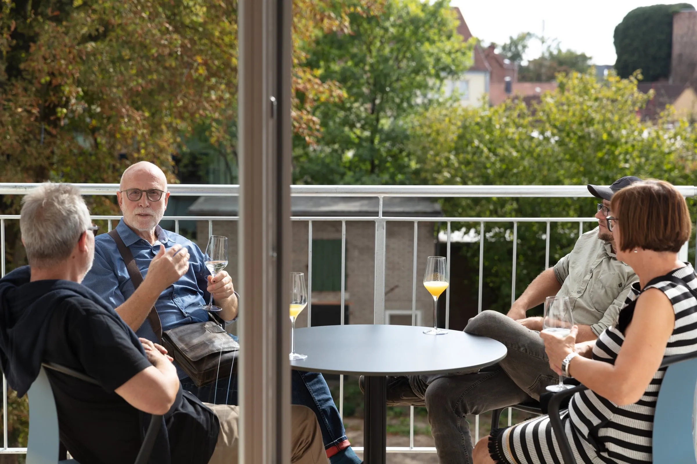Vier Gäste mit Gläsern sitzen an einem Tisch auf einem Balkon mit Blick ins Grüne