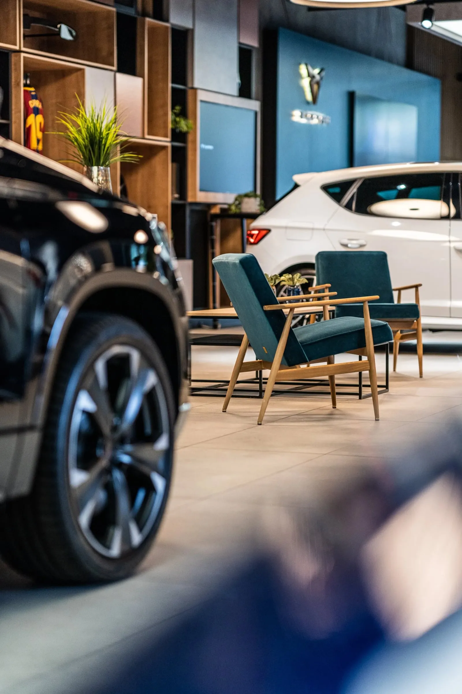 Showroom-Detail mit unscharfem schwarzem Fahrzeug links, dahinter zwei grüne Sessel und ein weißer Cupra