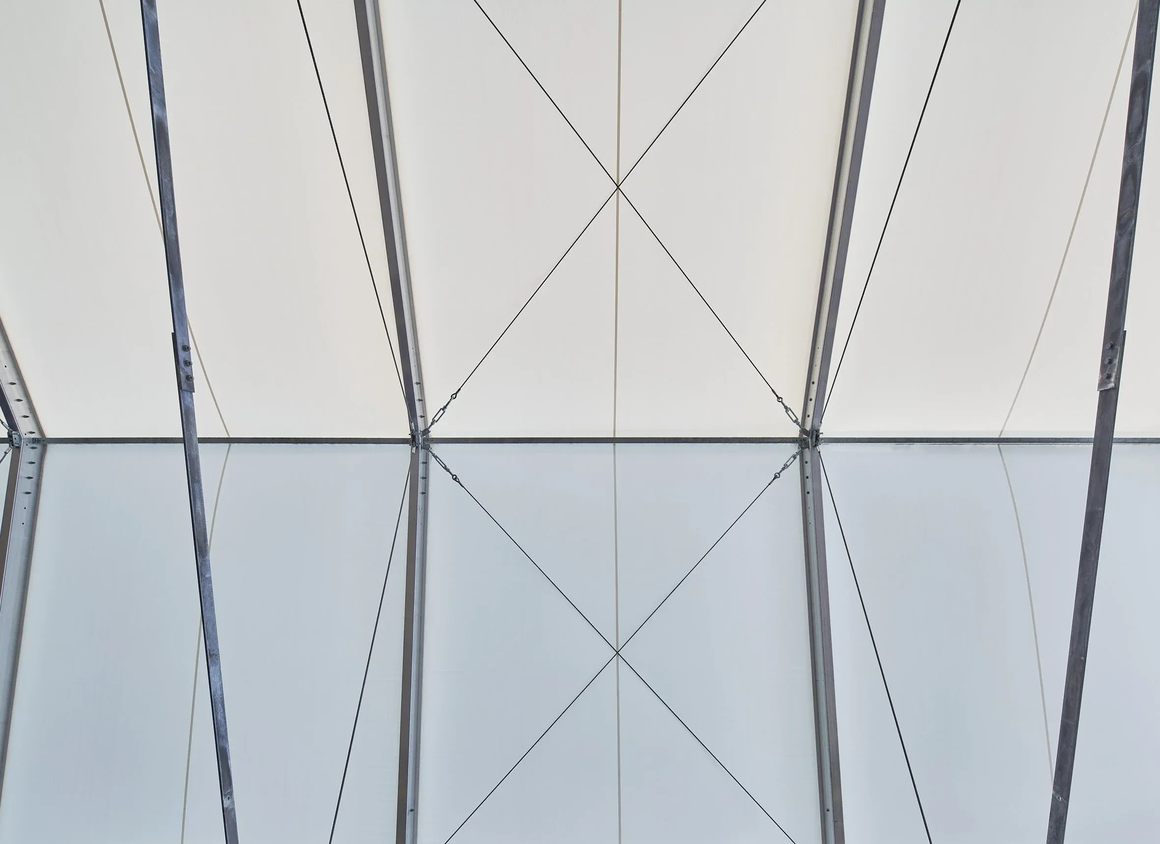 Detail innen, helle Zelthülle mit Stahlstützen und gekreuzten Stahlseilen der Hallenkonstruktion