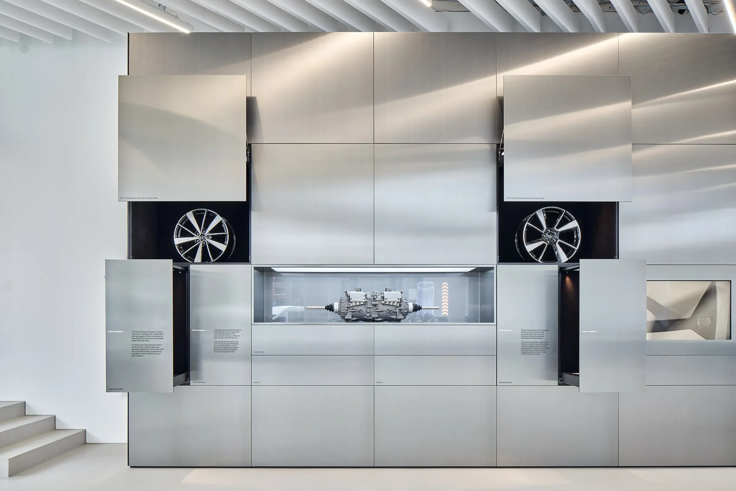 Innenraum, Materialwand mit aufgeklappten Paneelen, zwei Felgen und Antriebseinheit in der Vitrine