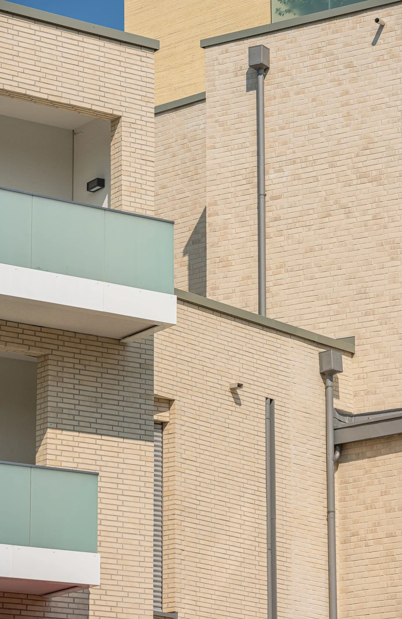 Außendetail der hellen Klinkerfassade eines Wohnbaus mit Balkonen und Glasgeländern, klares Tageslicht