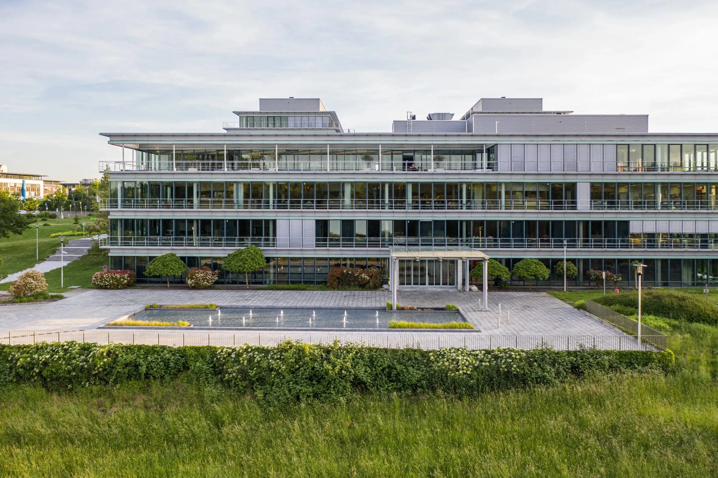Außenansicht des Accenture Campus mit gläserner Fassade, Wasserbecken und Vorplatz hinter einer Wiese