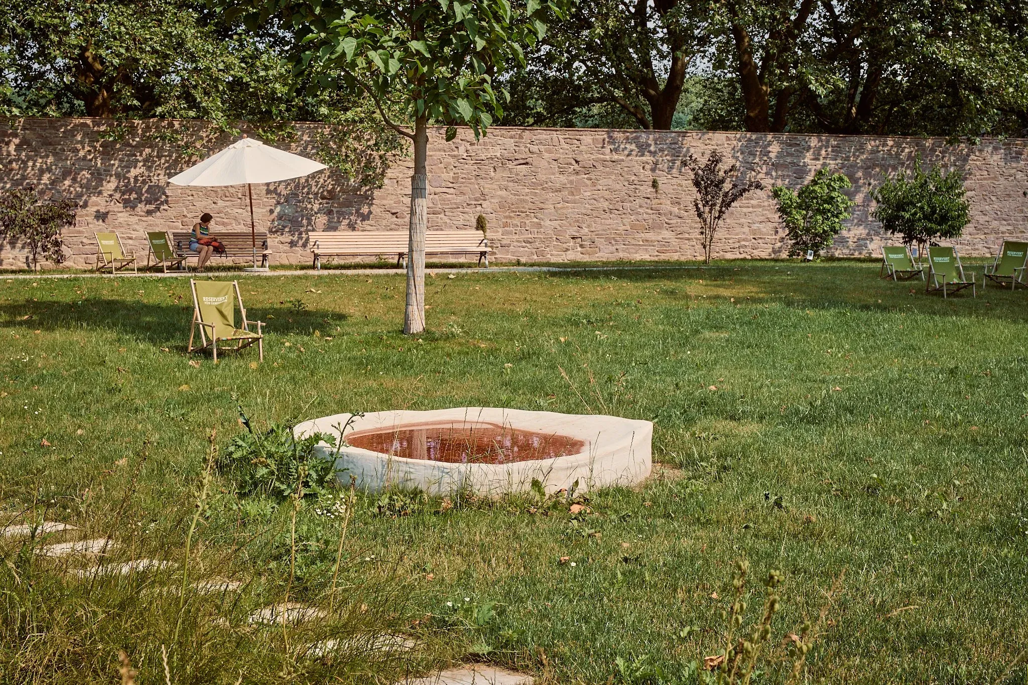 Liegestühle und Bank vor der alten Mauer im Remtergarten, runde Wasserschale im sommerlichen Rasen