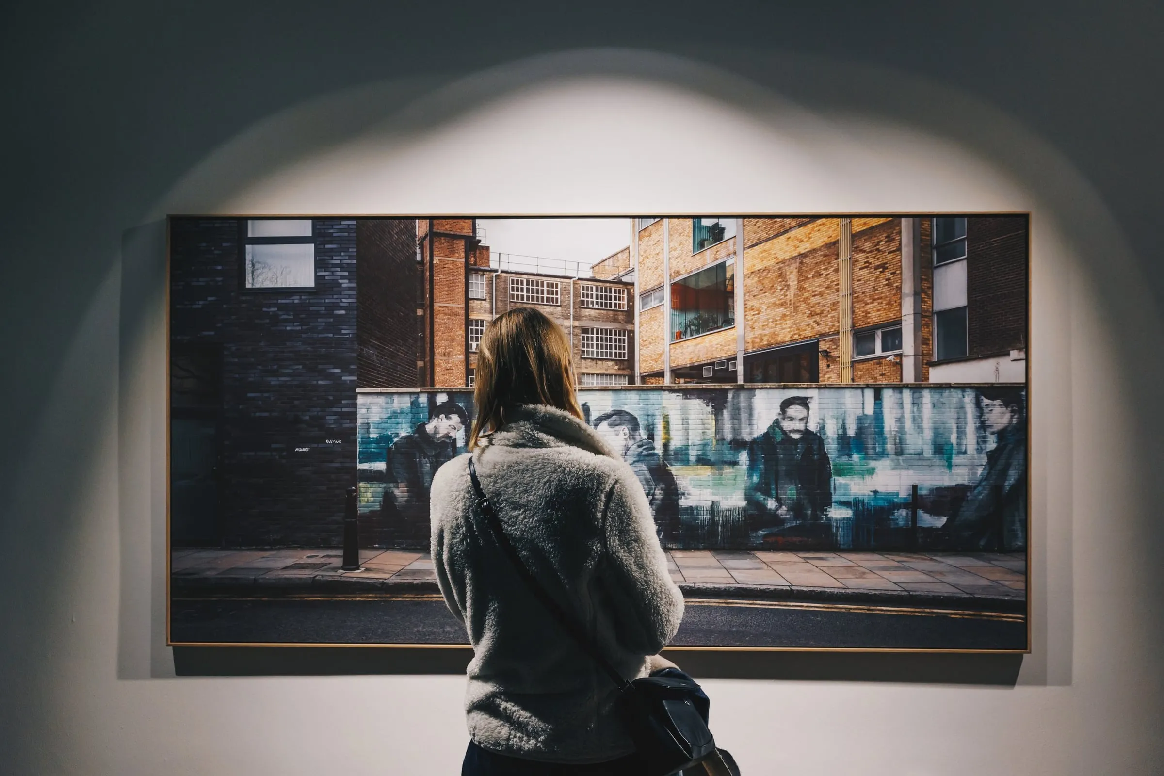 Frau von hinten betrachtet eine großformatige gerahmte Fotografie einer städtischen Straßenzeile an der Wand