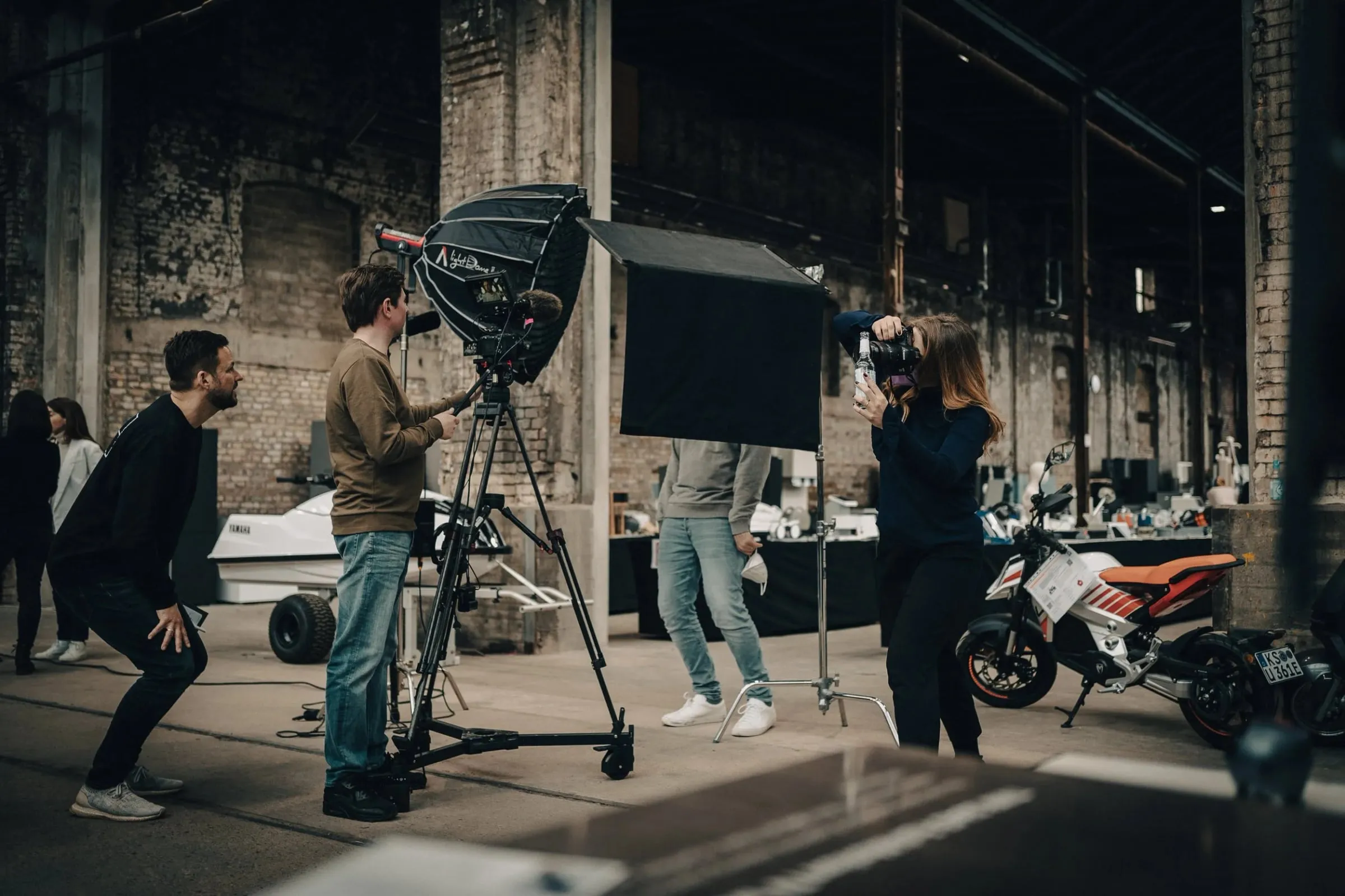 Filmteam mit Kamera, Stativ und Softbox bei Produktaufnahmen, Elektromotorrad und Helfer in der Halle