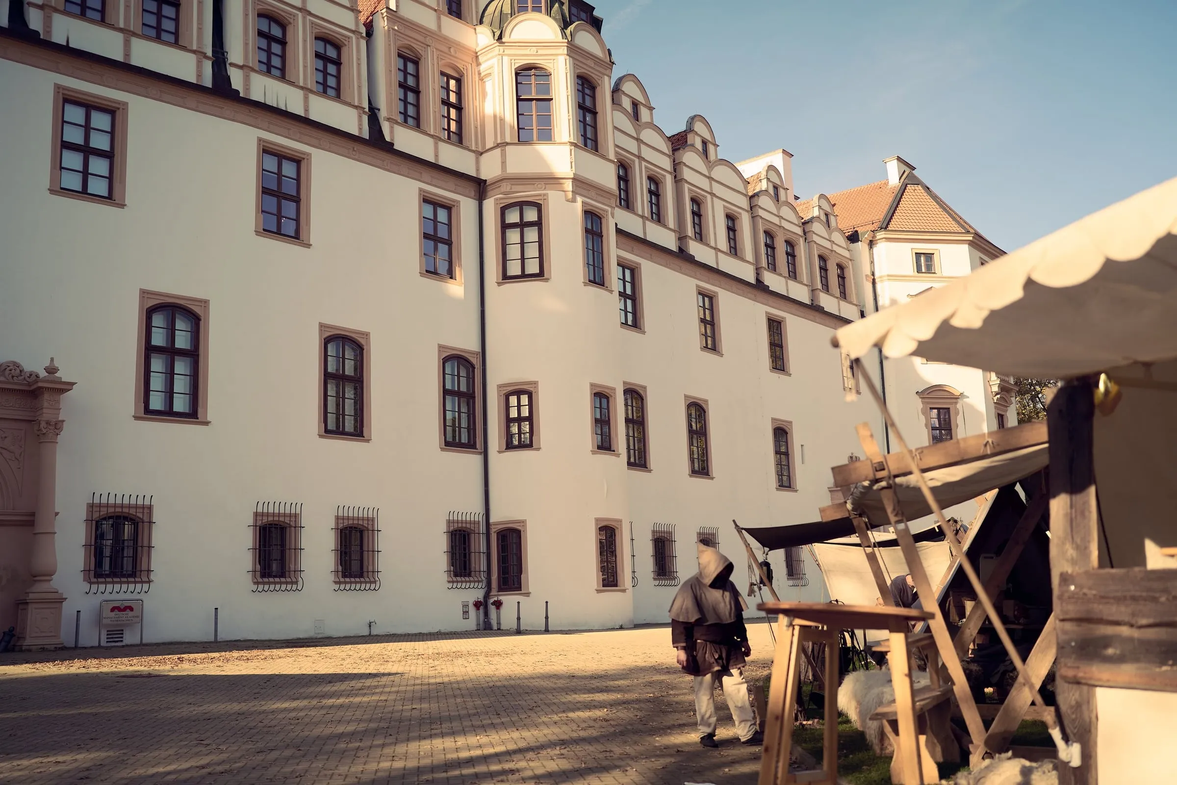 Helle Schlossfassade mit Sprossenfenstern, im Vordergrund eine Person und ein Marktstand