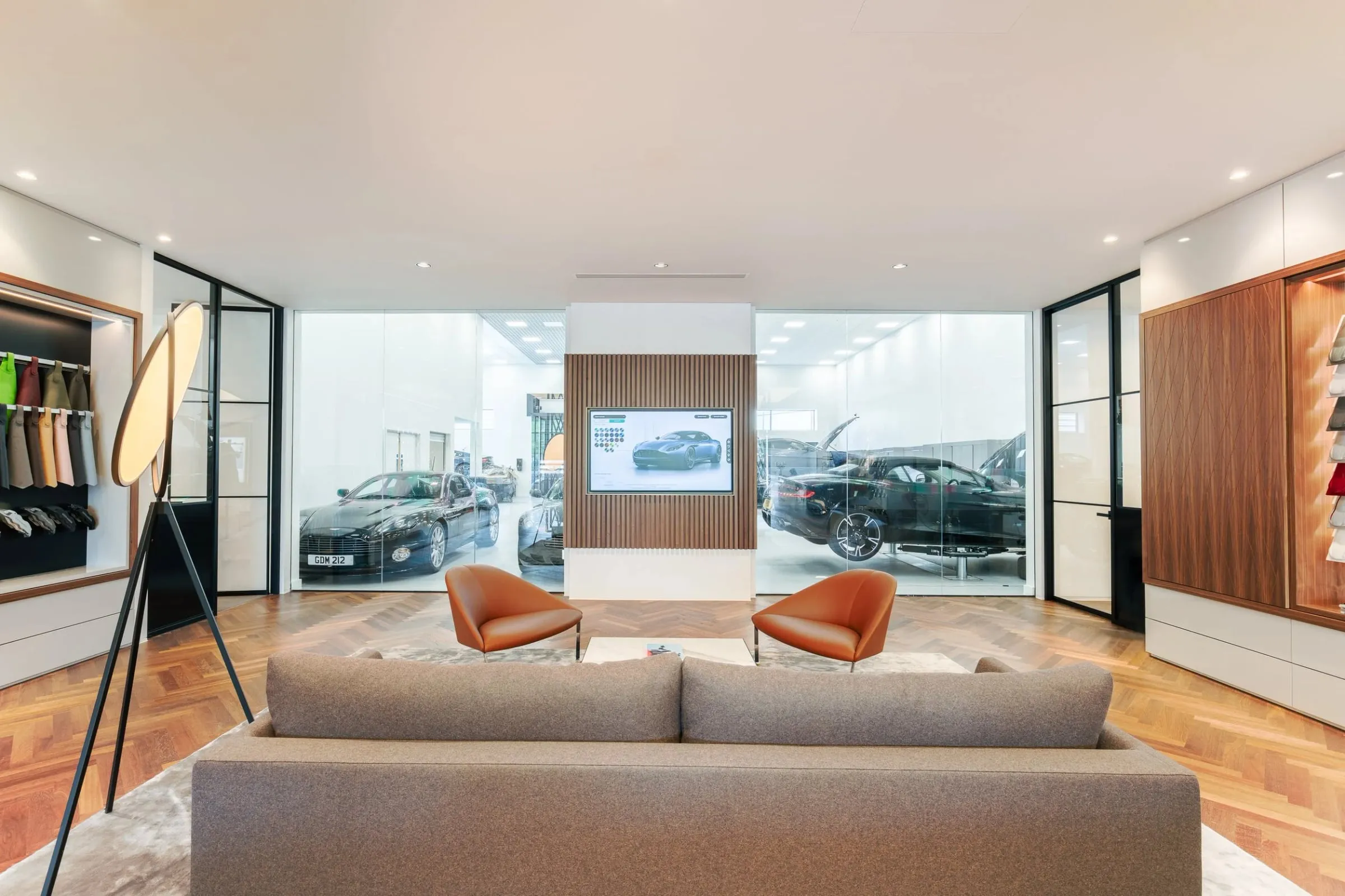Innenraum-Lounge mit Sofa und Sesseln, Blick durch große Glasfront auf Fahrzeuge im angrenzenden Showroom