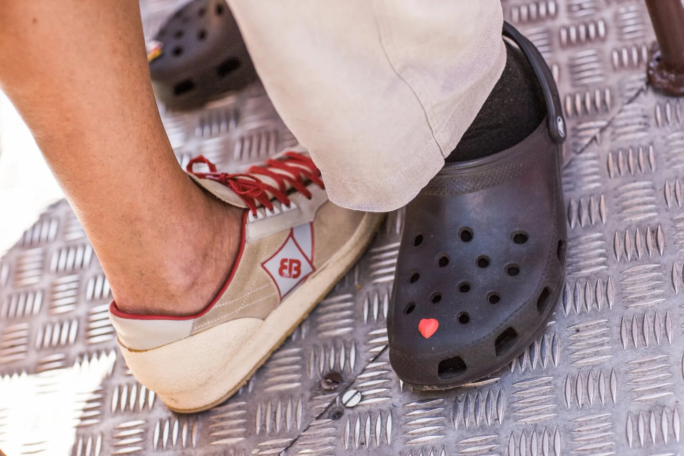 Detailaufnahme zweier Füße auf Riffelblech, ein Sneaker und ein dunkler Clog nebeneinander