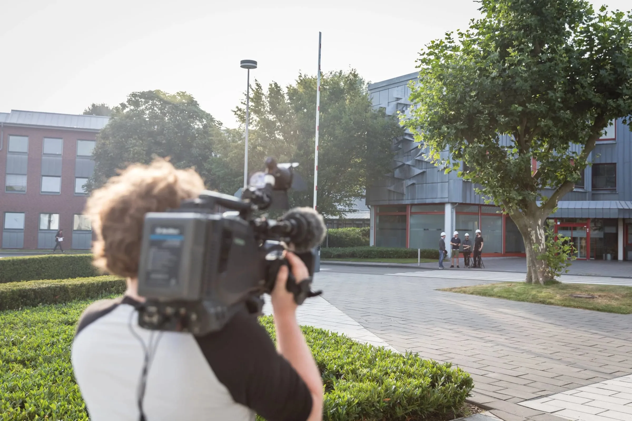 Kameramann filmt von hinten das Rheinzink-Werksgelände mit Gebäuden, Bäumen und einer Personengruppe, Außenaufnahme