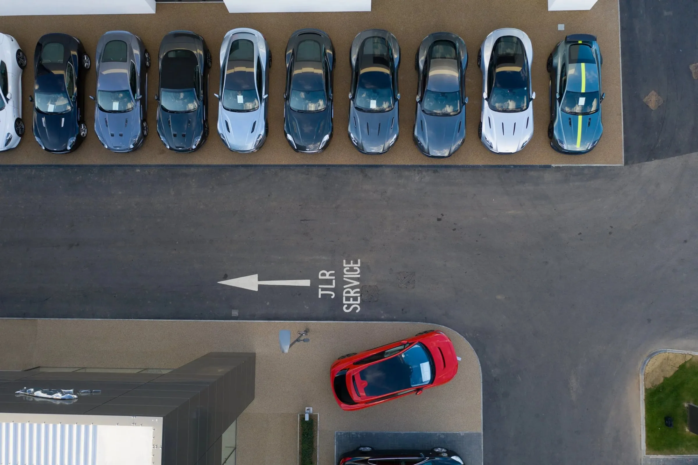 Luftaufnahme einer Fahrzeugreihe auf dem Parkplatz von oben, Fahrbahnmarkierung und ein rotes Auto