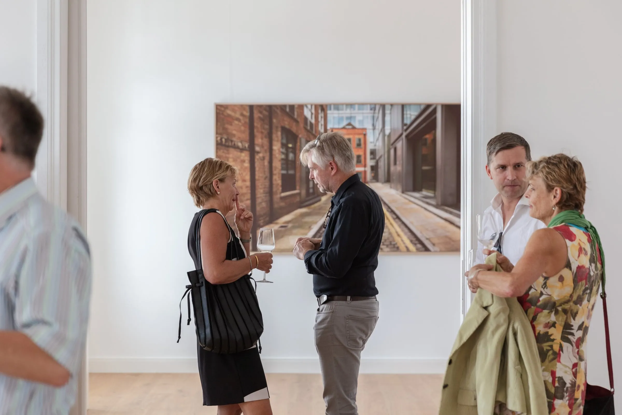 Gäste mit Weingläsern im Gespräch vor großformatiger gerahmter Fotografie einer urbanen Straße