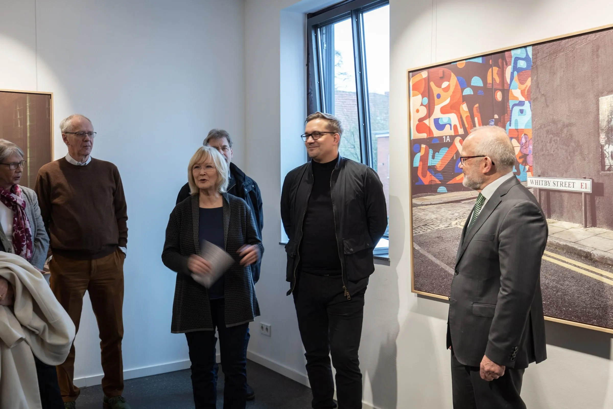 Gruppe hört einer Frau mit Redekarte zu, rechts eine großformatige Fotografie mit Straßenschild Whitby Street